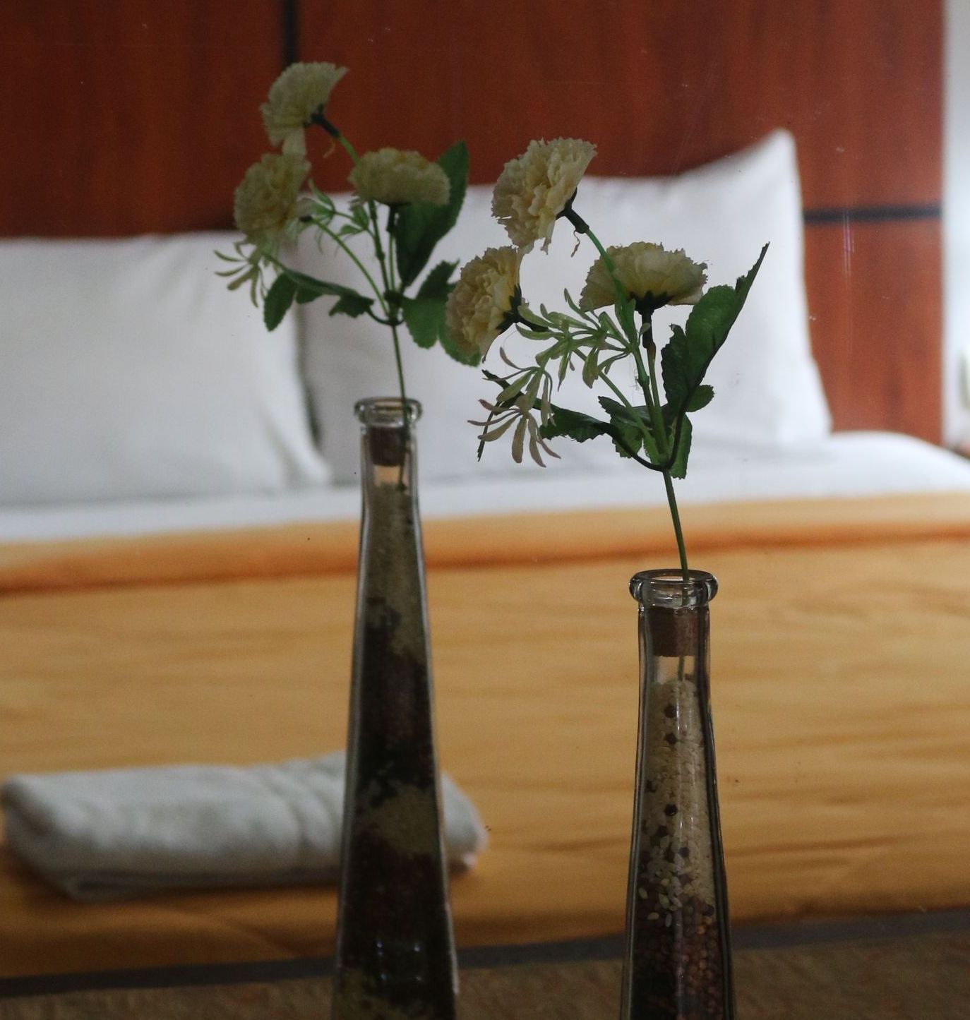 Dos jarrones con flores delante de una cama.