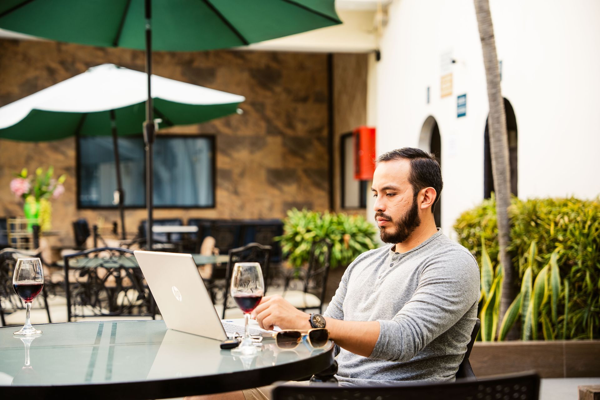 Un hombre está sentado en una mesa con una computadora portátil y una copa de vino.