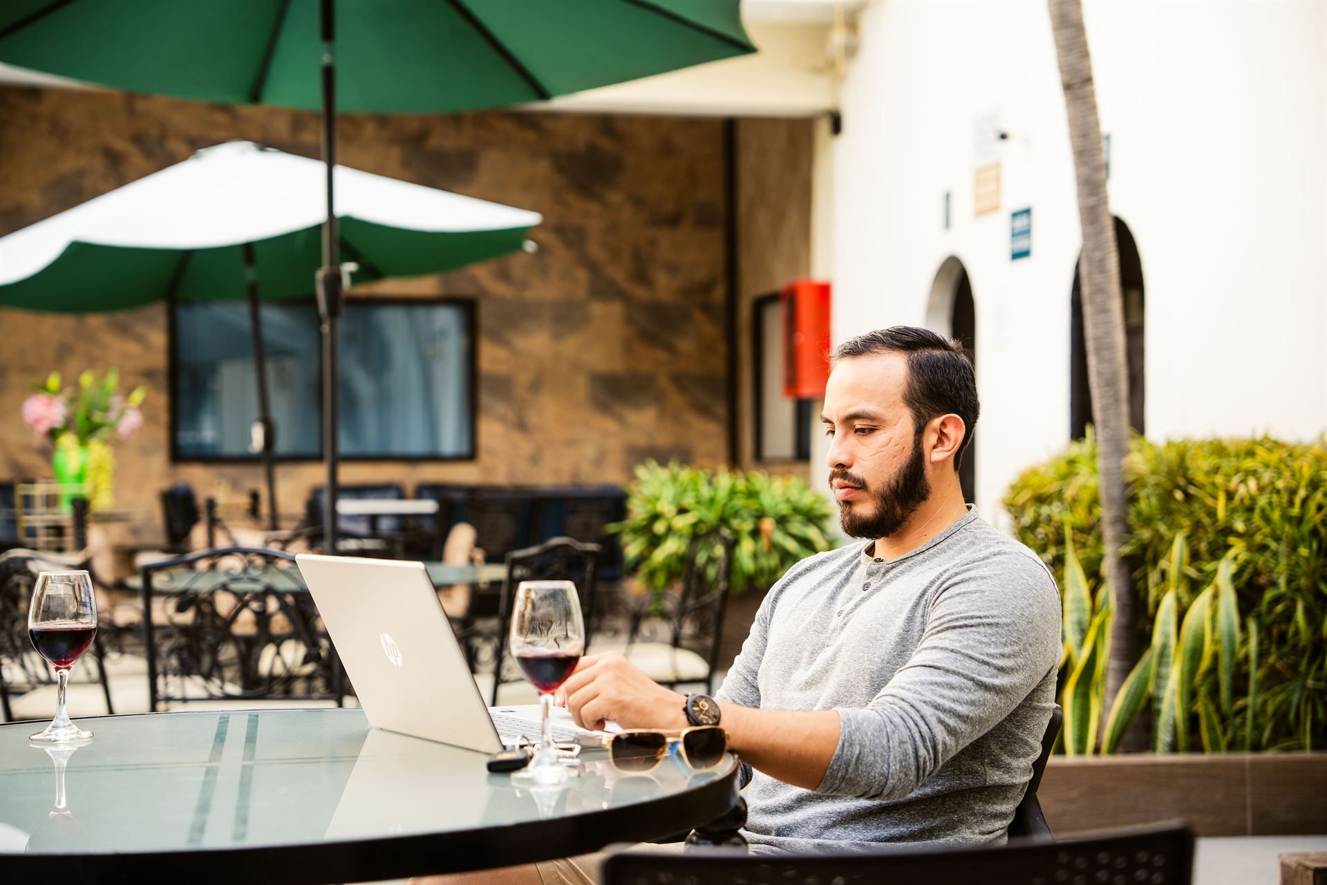 Un hombre está sentado en una mesa con una computadora portátil y una copa de vino.