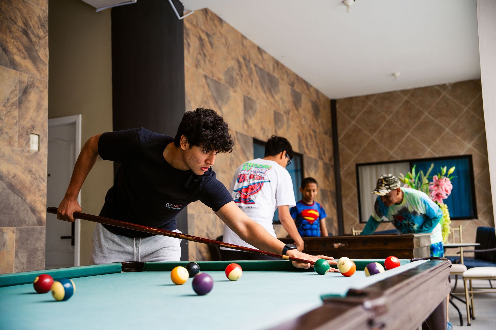 Un hombre está jugando al billar en una habitación con otras personas.