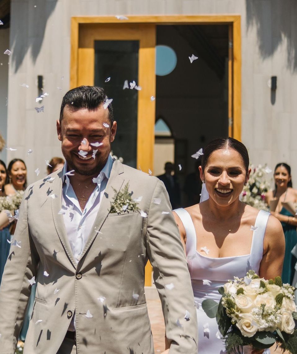 Una novia y un novio están parados frente a un edificio con confeti cayendo sobre ellos.