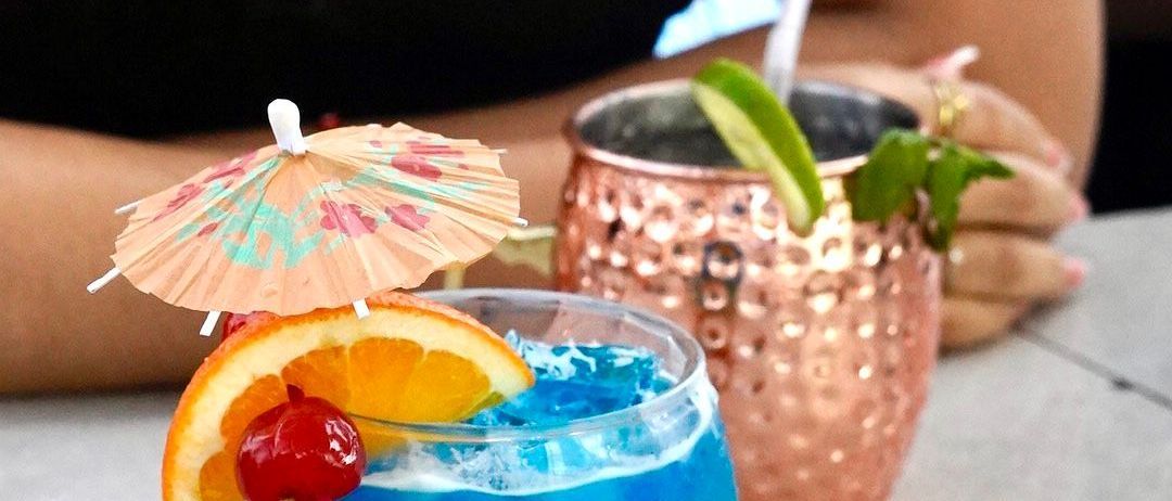 Una persona está sentada en una mesa con dos bebidas con sombrillas encima.