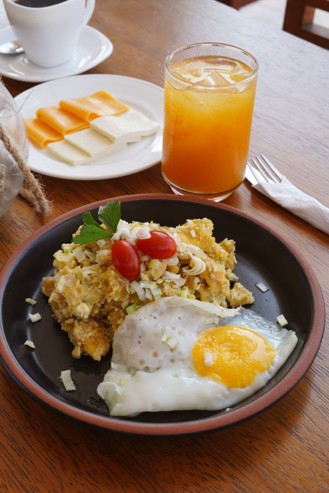Un plato de comida con huevos, tomates y un vaso de jugo de naranja sobre una mesa.