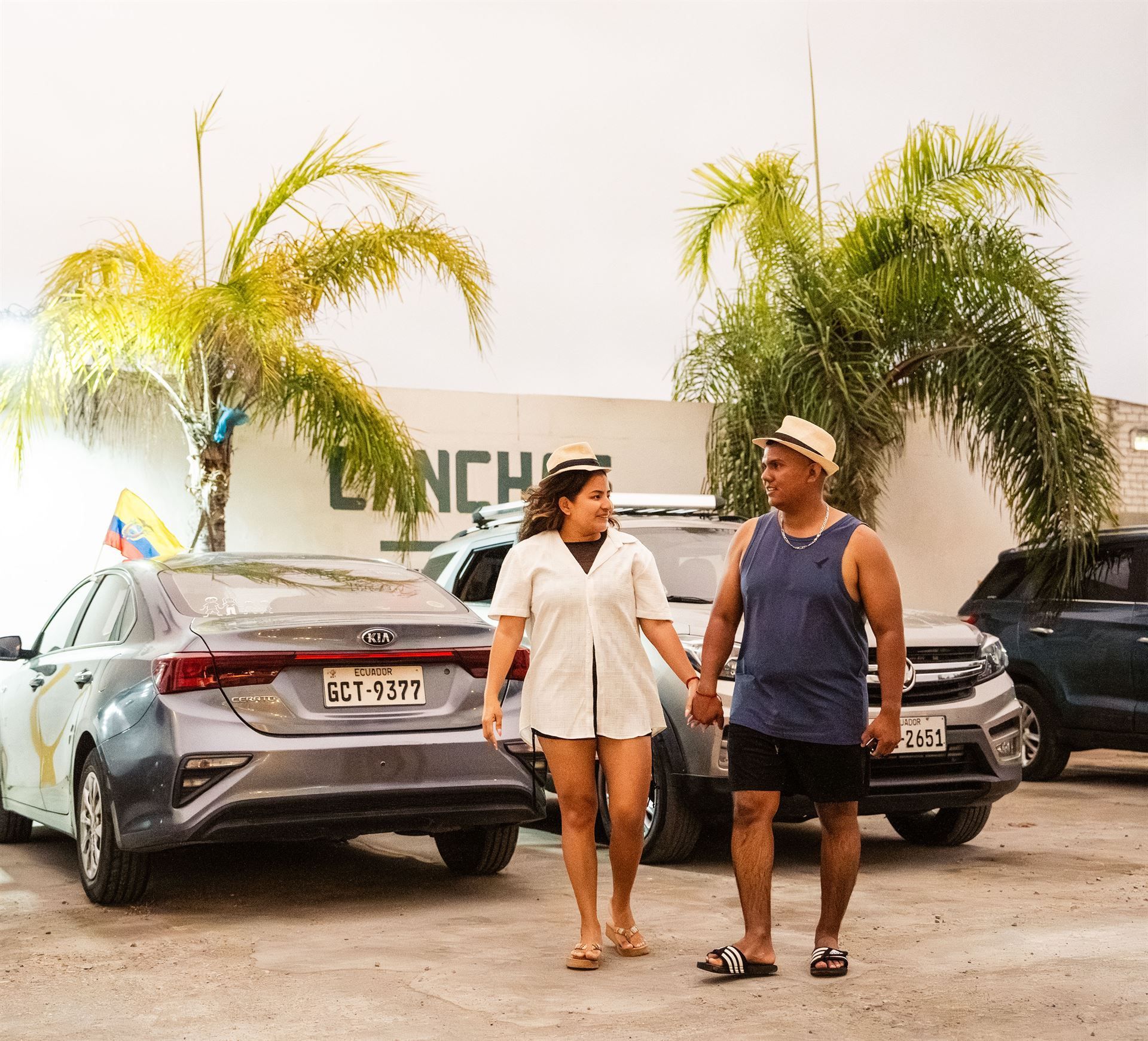 Un hombre y una mujer caminan en un estacionamiento tomados de la mano.