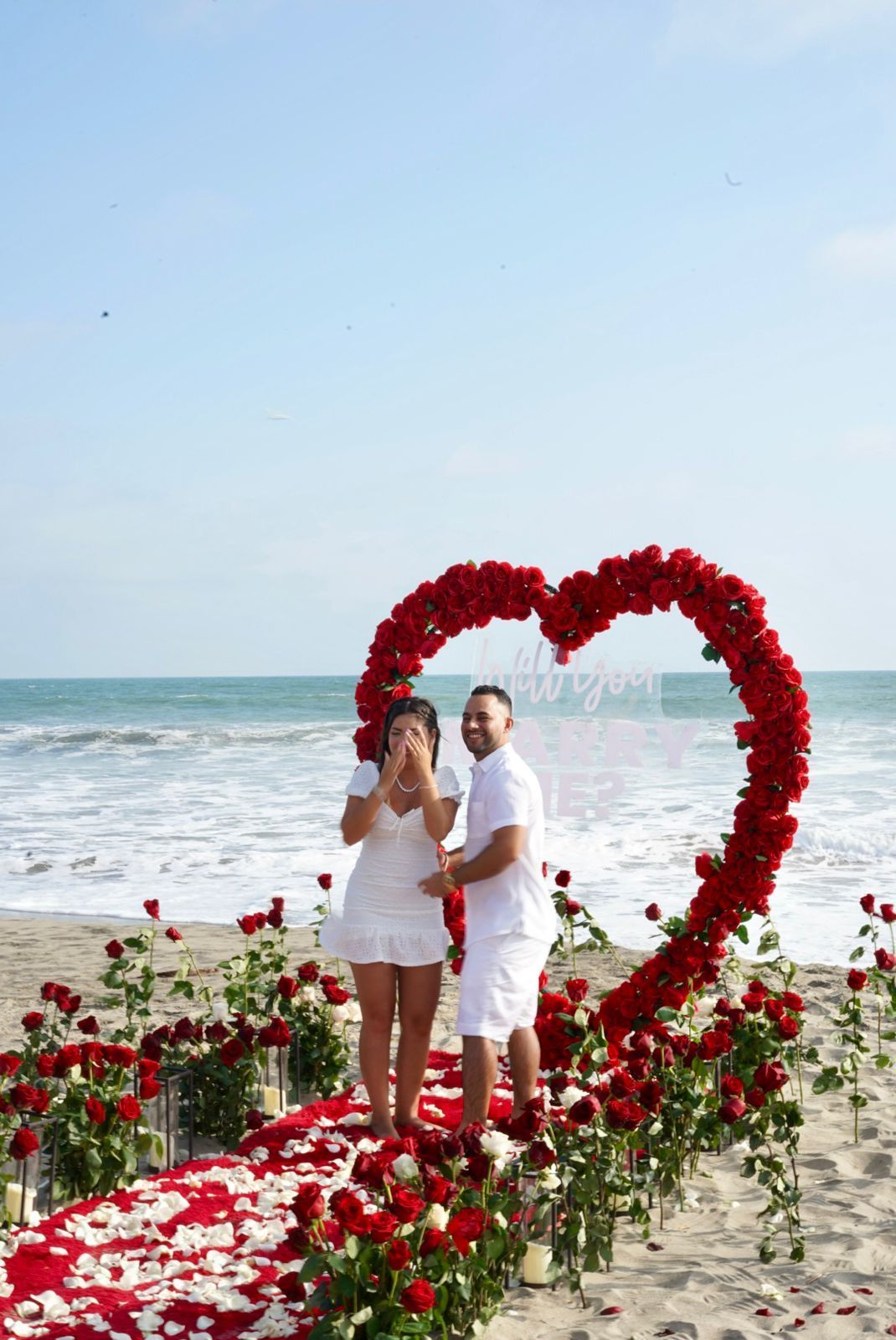 Un hombre y una mujer están parados frente a un arco en forma de corazón en la playa.