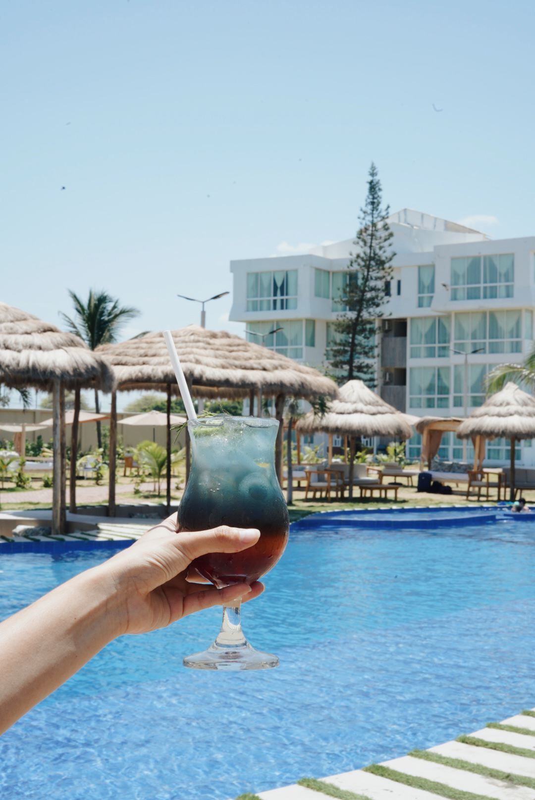 Una persona sostiene una bebida frente a una piscina.