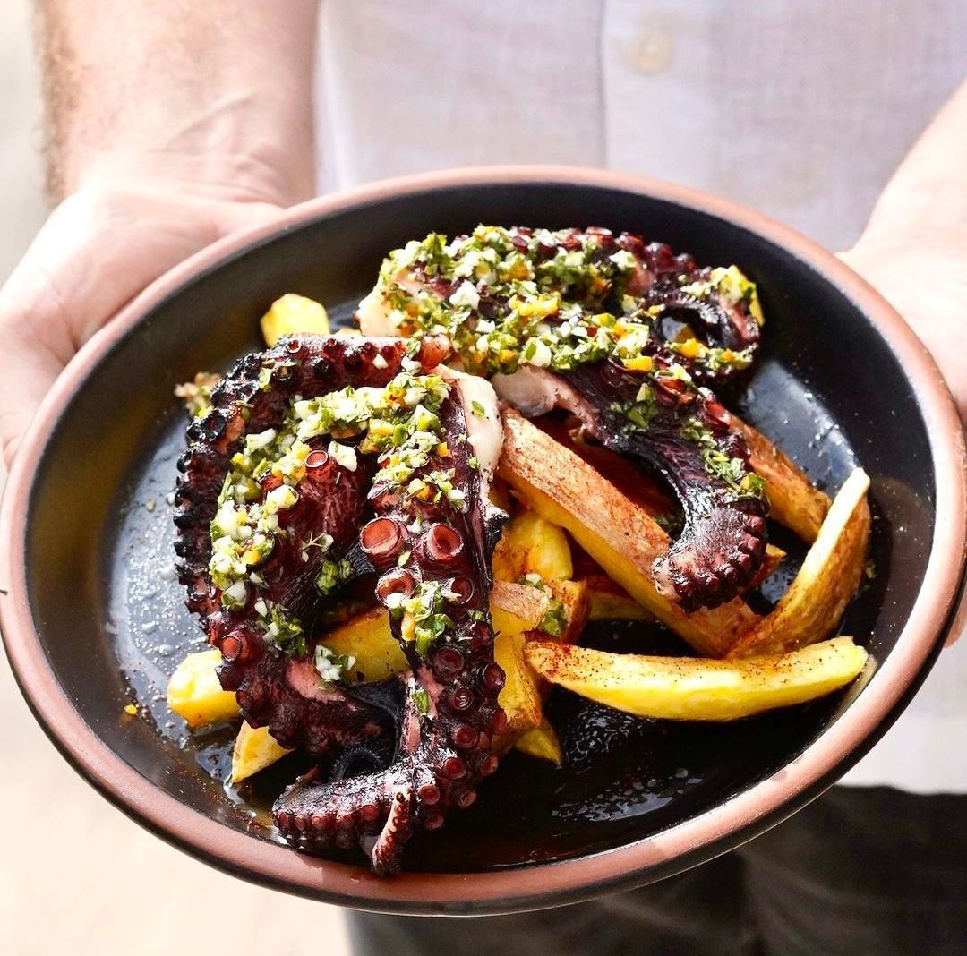 Una persona sostiene un tazón de pulpo y papas fritas.