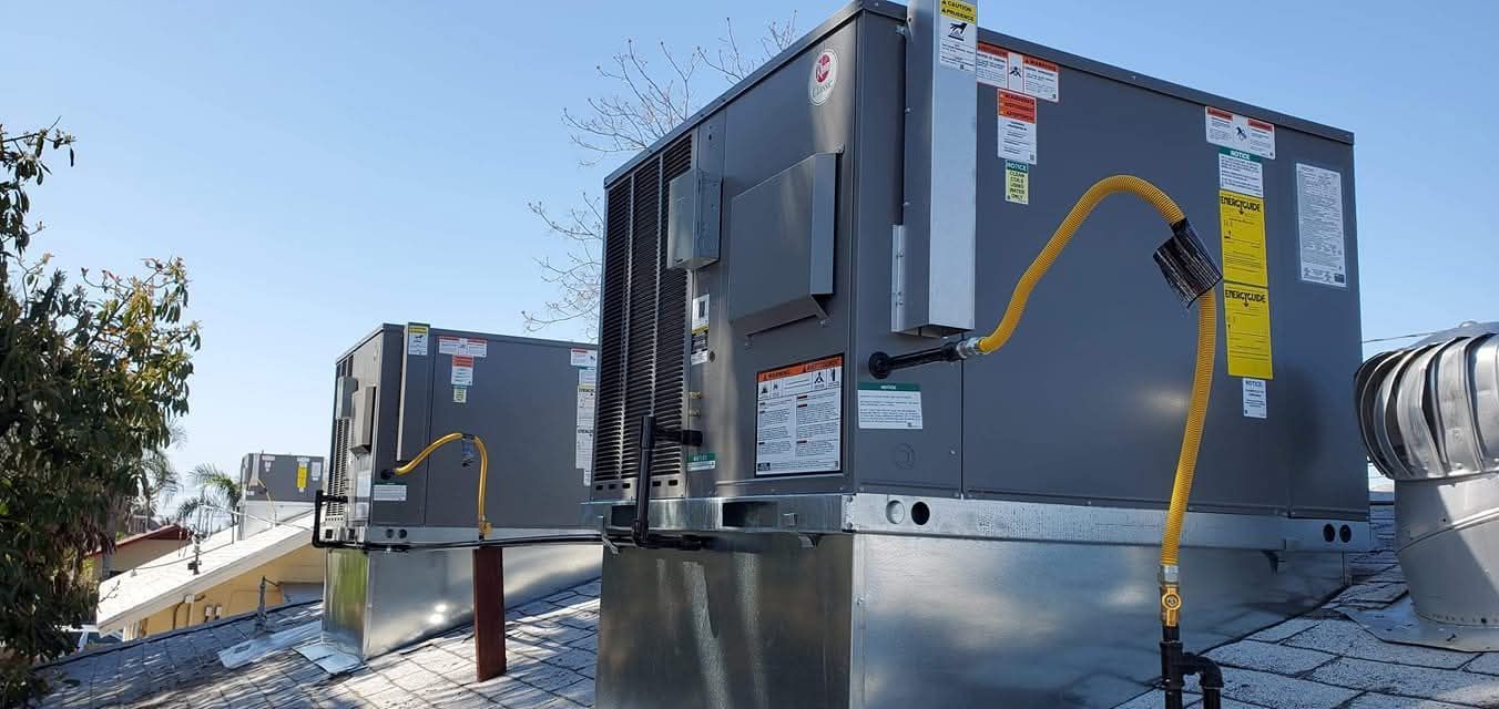 A row of air conditioners are sitting on top of a snow covered roof.