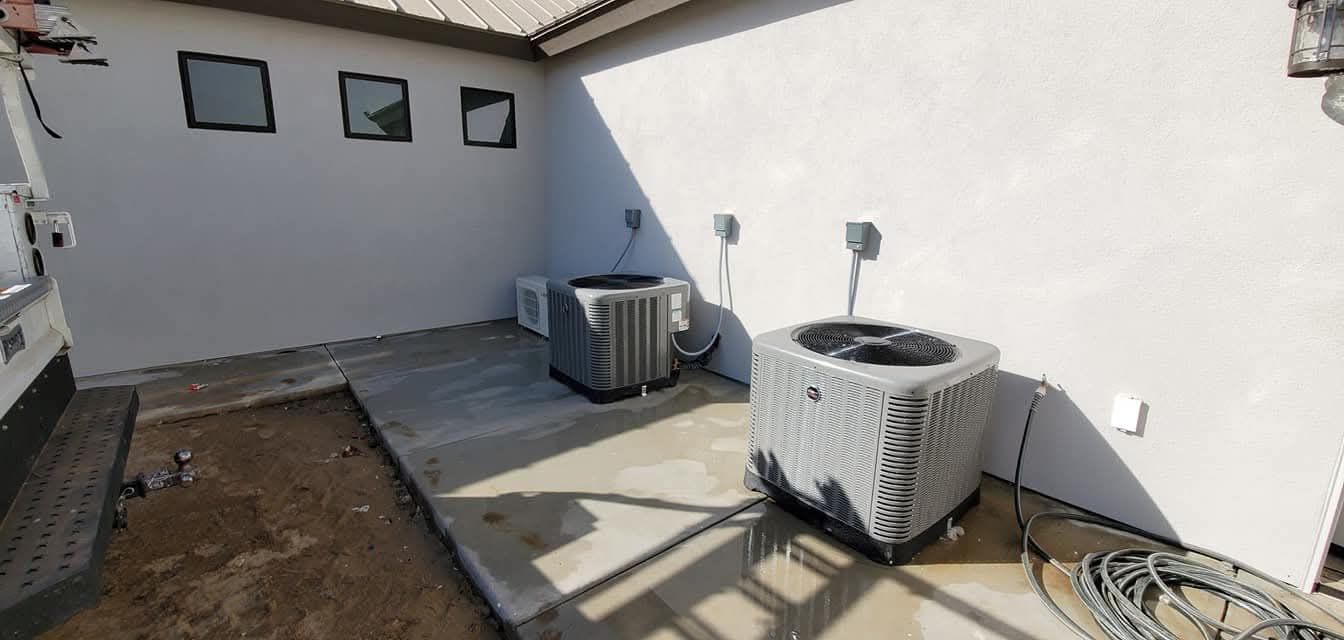 There are two air conditioners in the backyard of a house.
