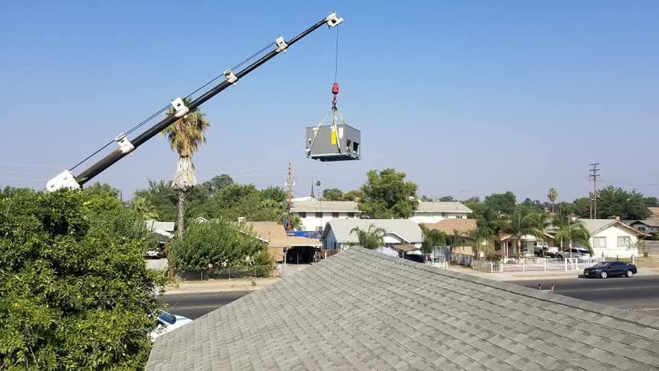 A crane is lifting an air conditioner on top of a roof.