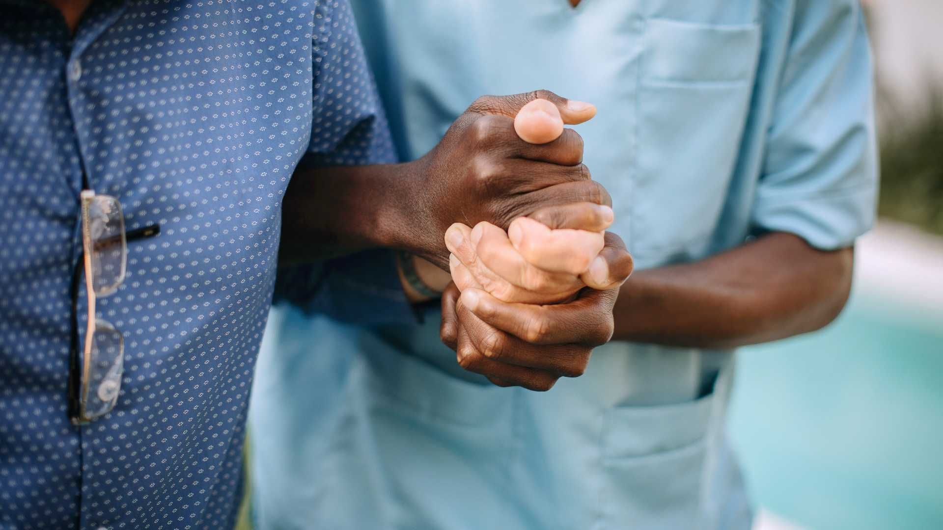 A nurse is holding the hand of an elderly man.