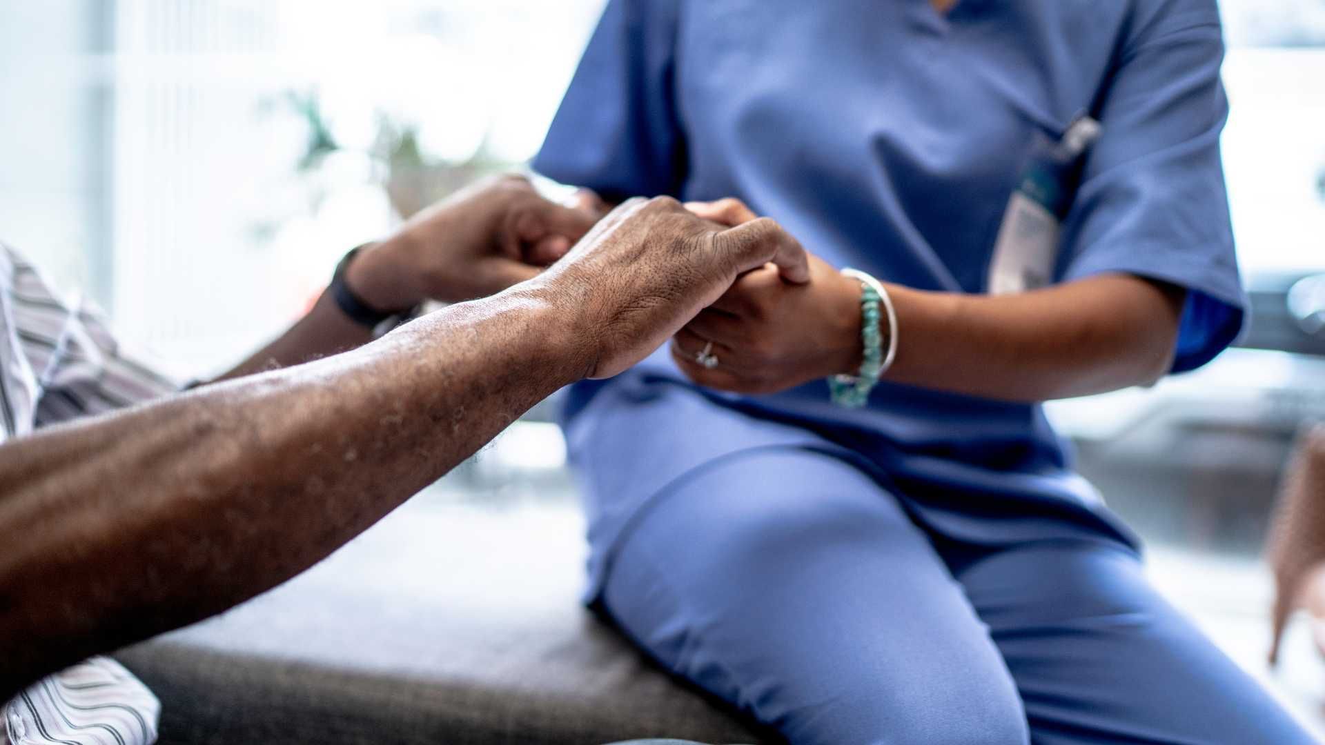 A nurse is holding the hand of an elderly man.