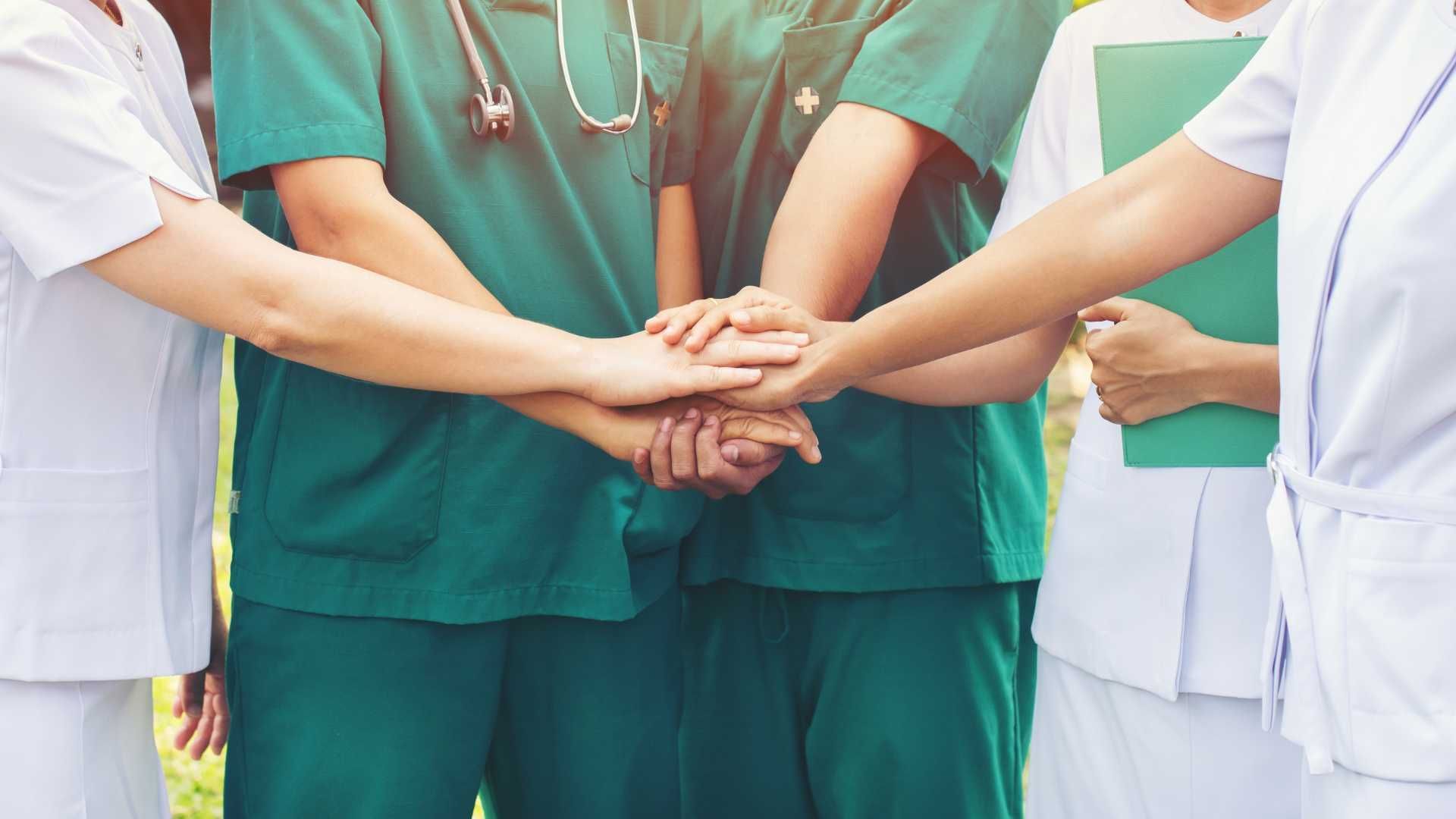 A group of doctors and nurses are putting their hands together.