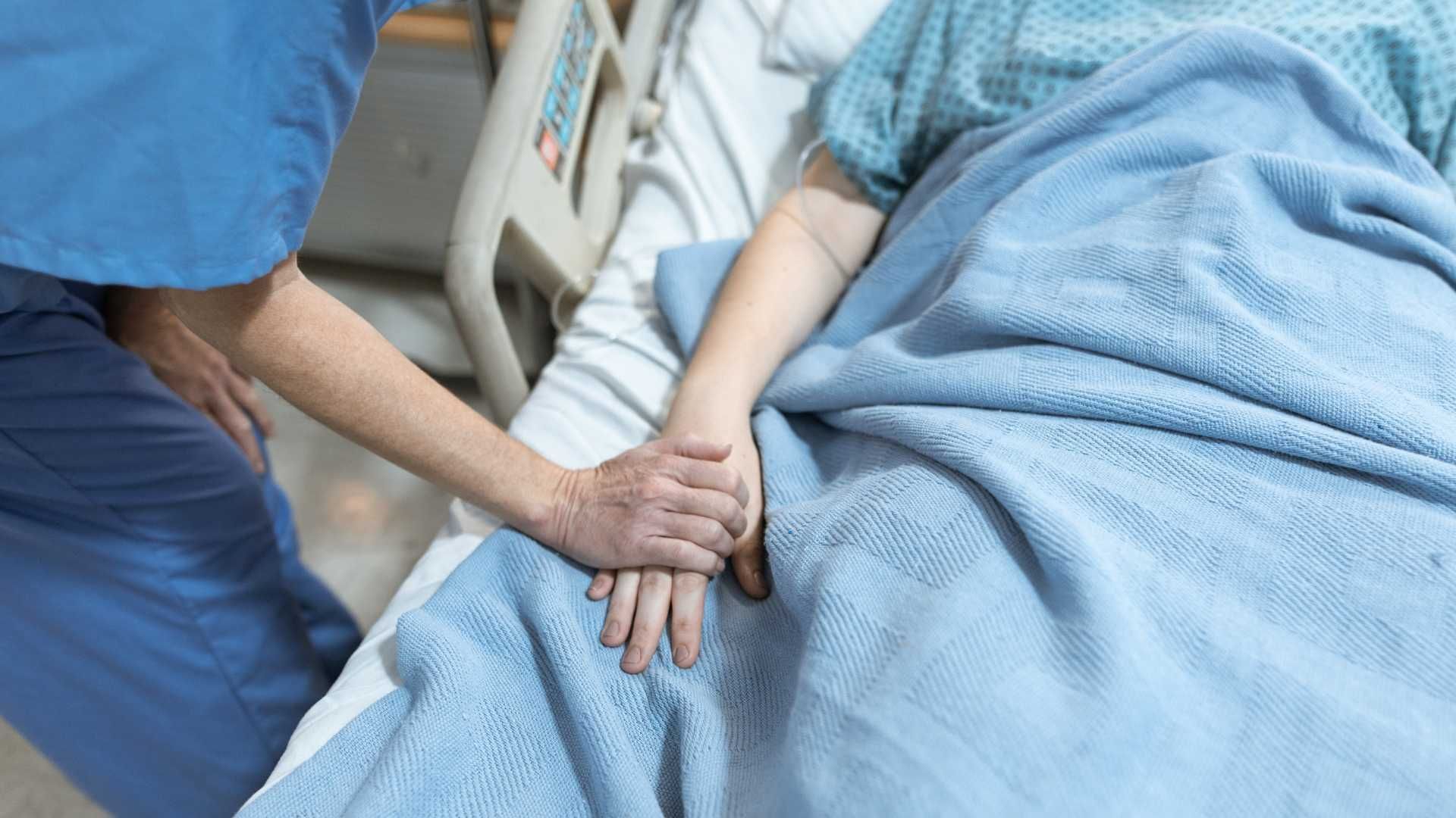 A nurse is holding the hand of a patient in a hospital bed.