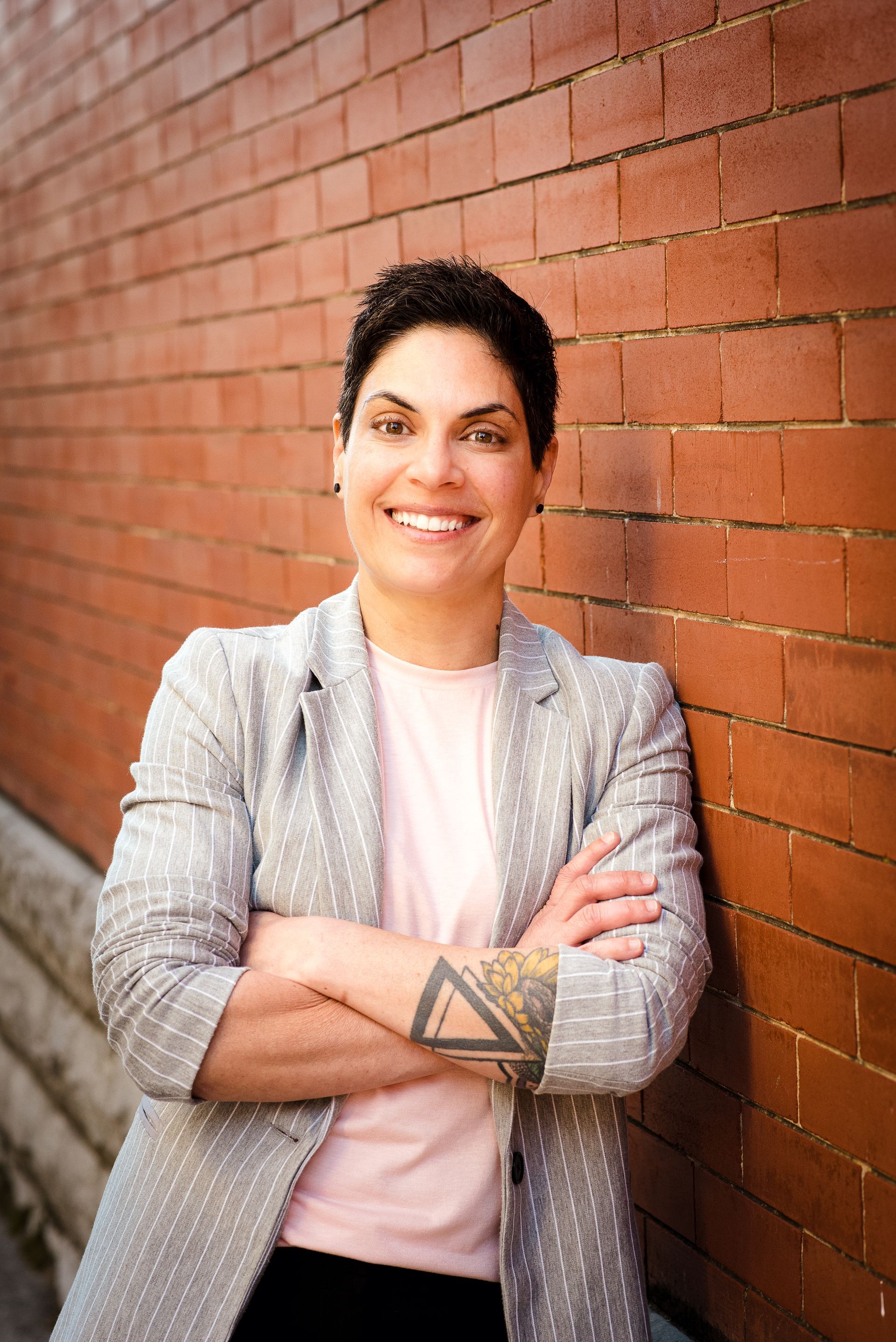 A woman is standing in front of a brick wall with her arms crossed.