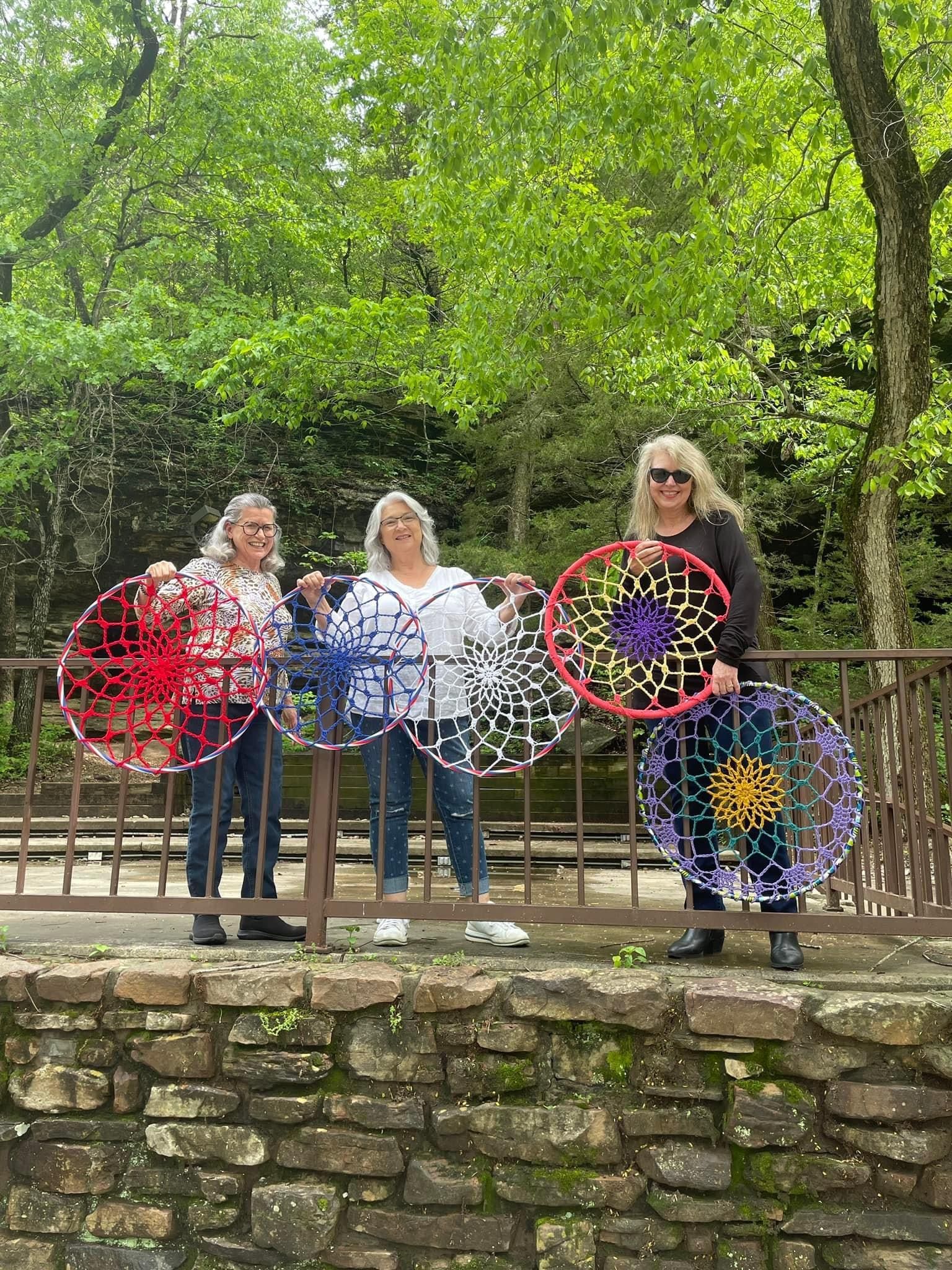 Three women are standing next to each other holding dream catchers.