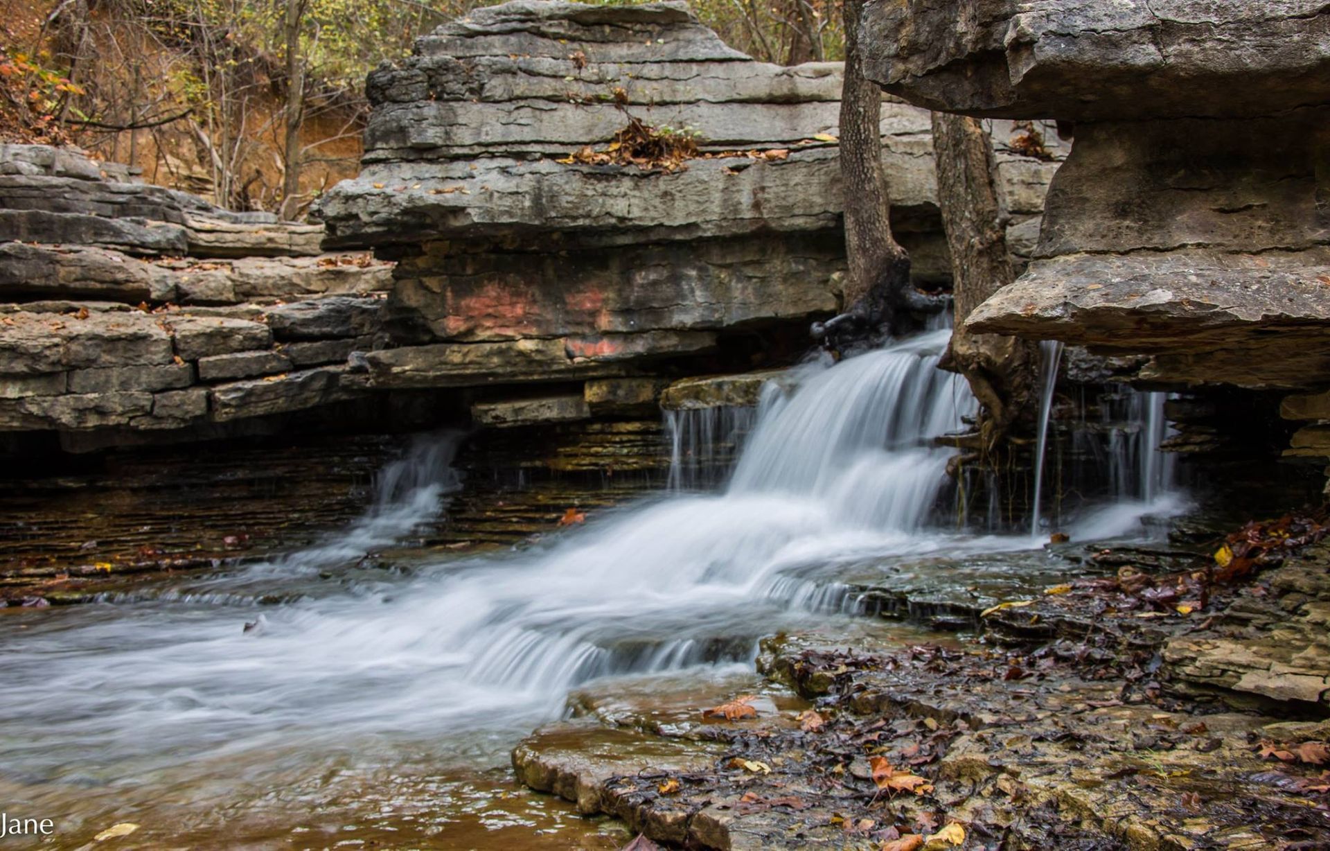 A small waterfall is surrounded by rocks in the woods.