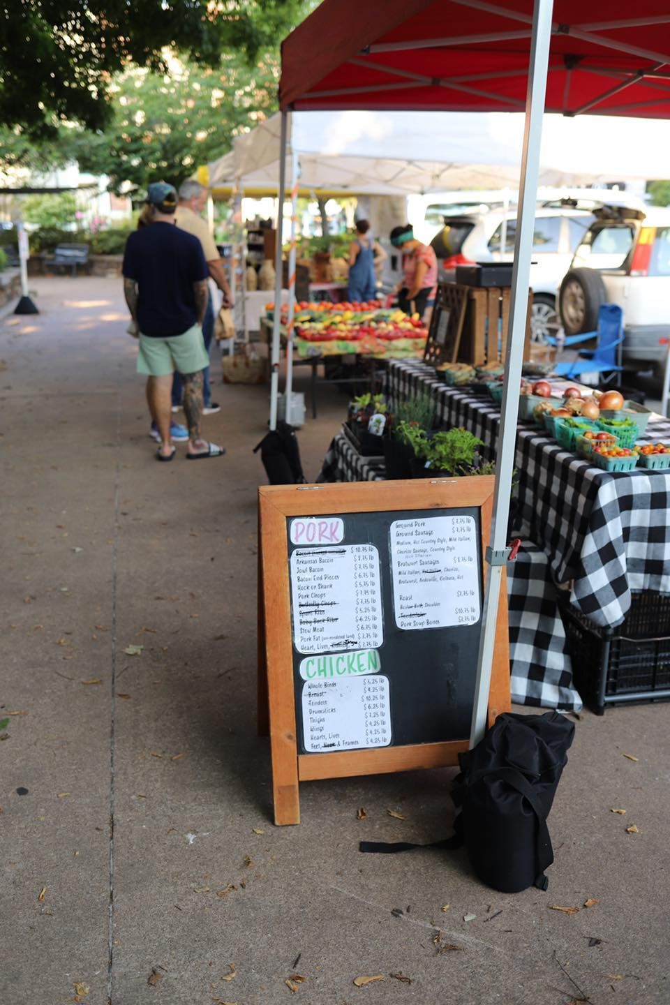 A chalkboard with a menu on it sits next to a table at a farmers market.