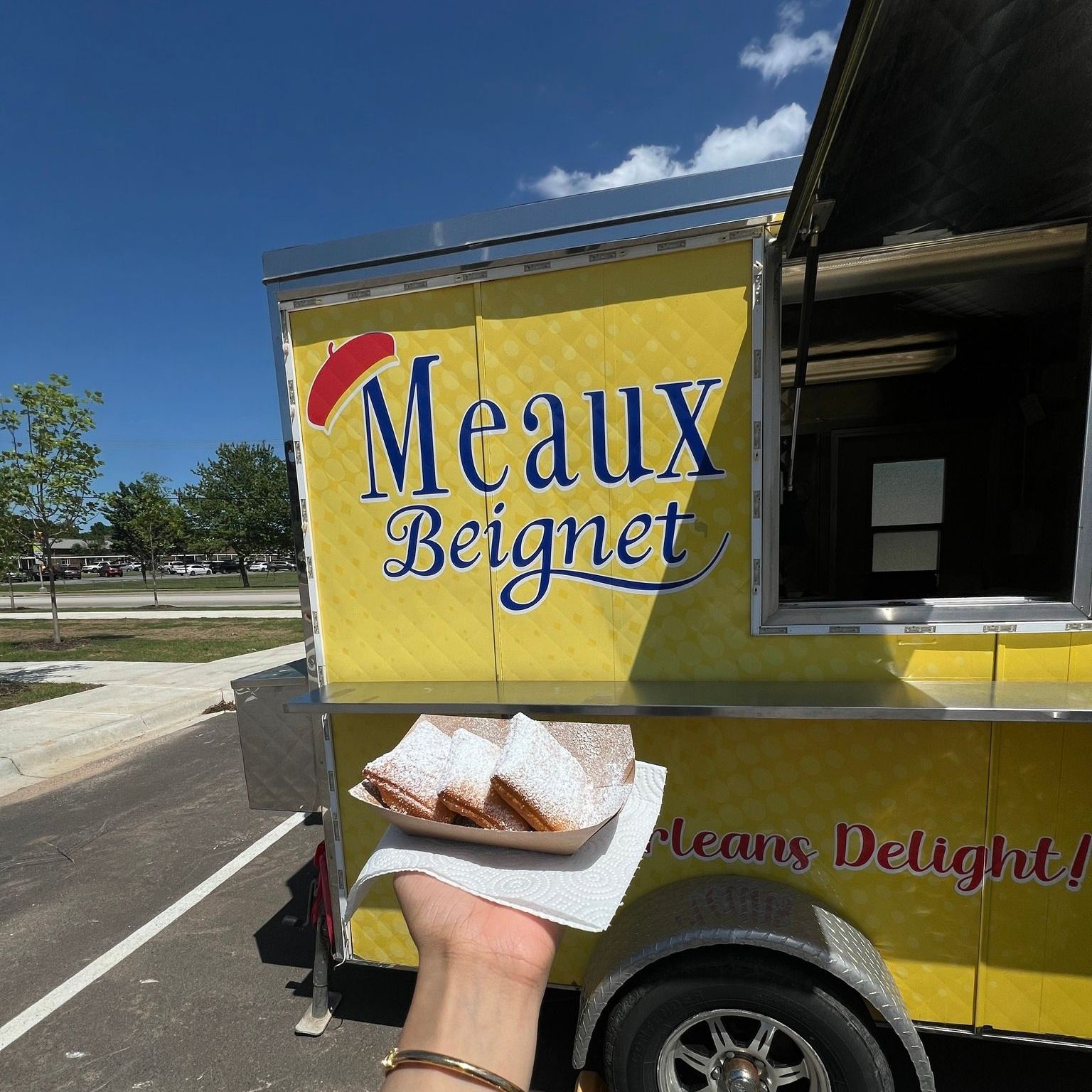 A person holding a plate of food in front of a meaux beignet food truck