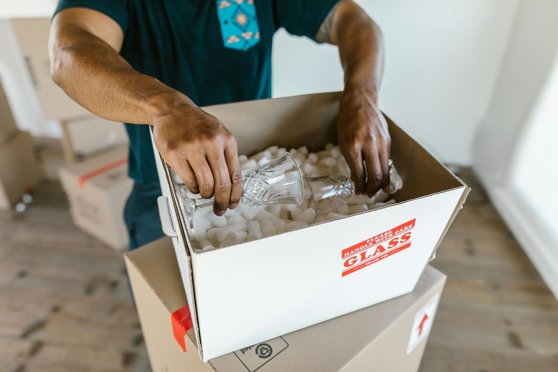 Person packing bubble-wrapped items into a white shipping box on a table