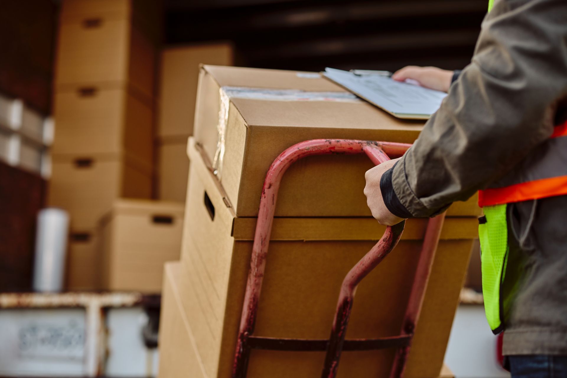 Worker loading a cardboard box onto a hand truck in a warehouse loading area