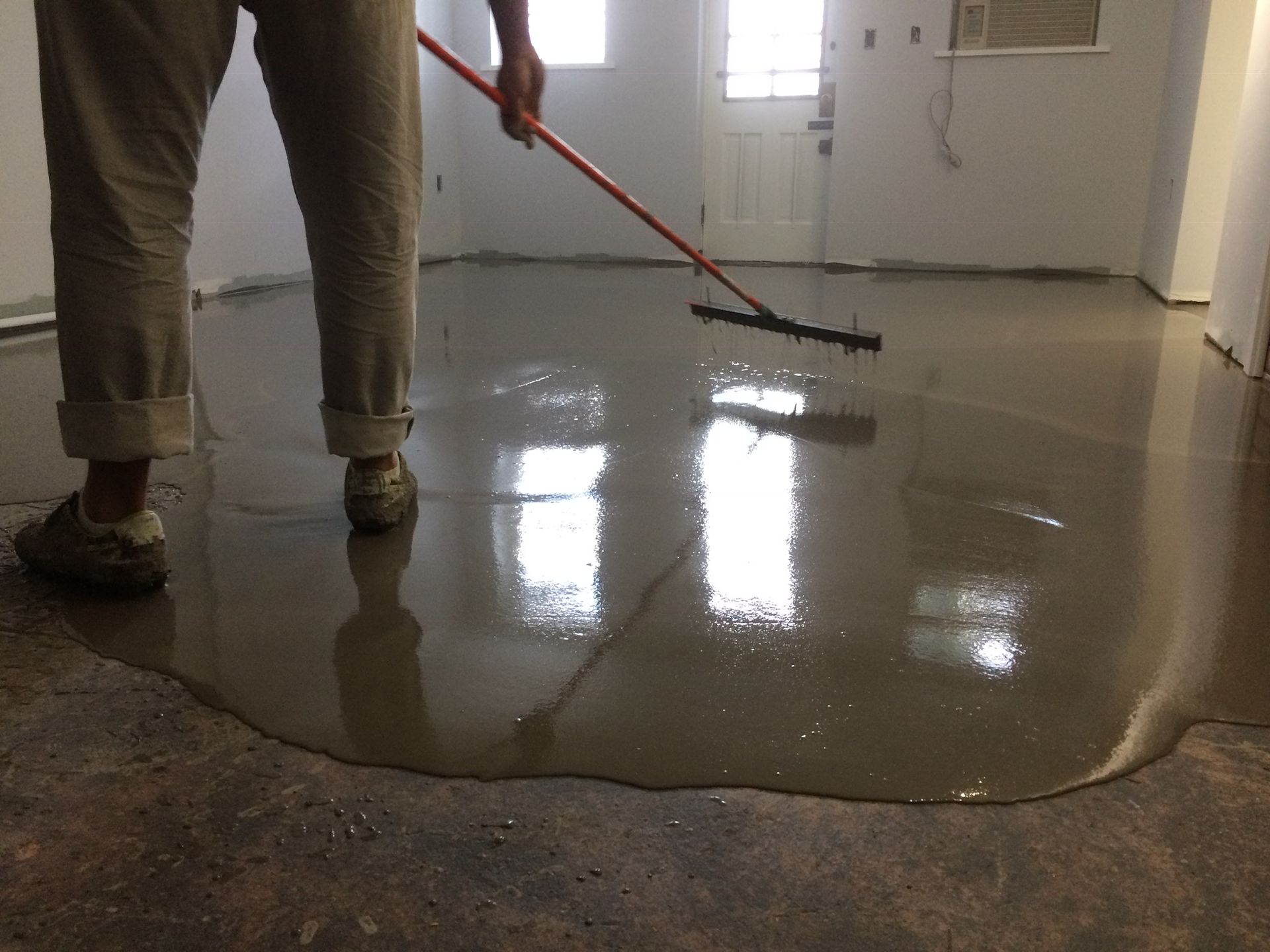 A person is spreading concrete on the floor with a broom.