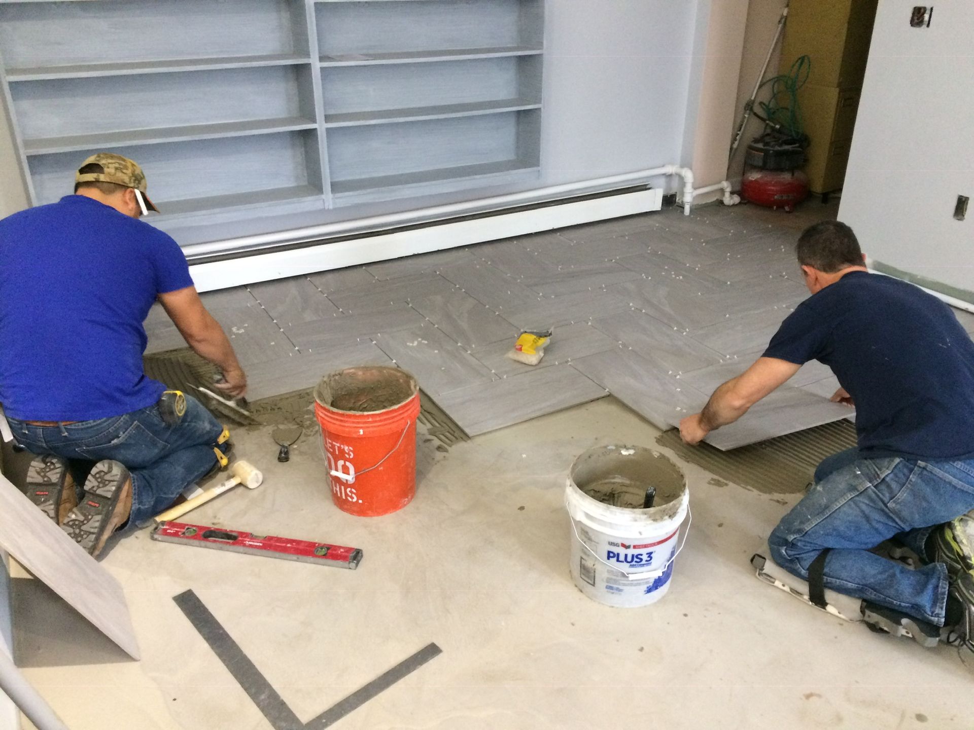 Two men are working on a tile floor in a room.