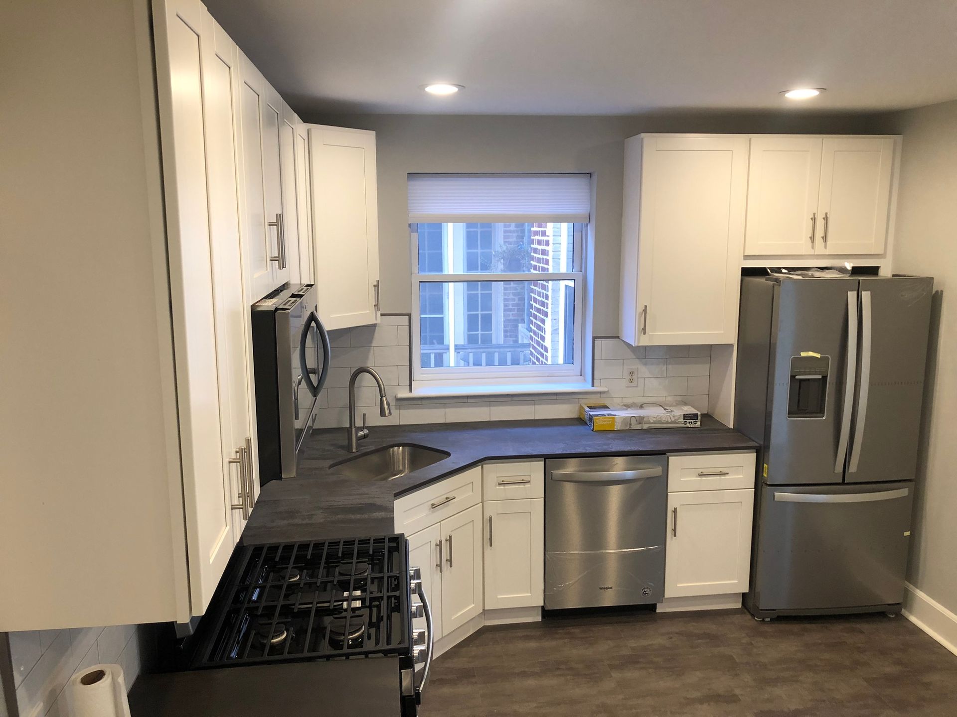 A kitchen with white cabinets , a stove , a refrigerator , a sink , and a window.