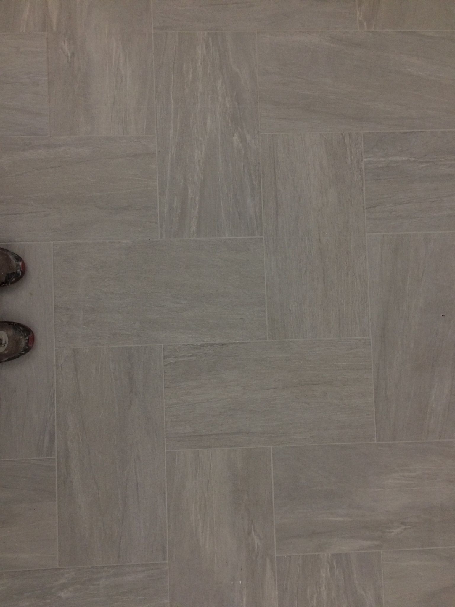 A person 's feet are standing on a tiled floor.