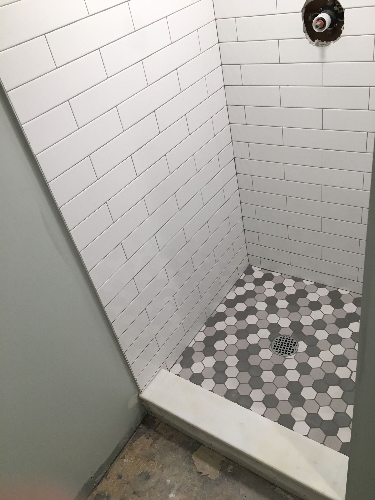 A shower with white tiles and a hexagon floor
