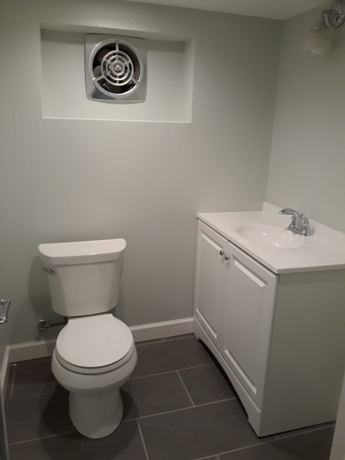 A bathroom with a toilet , sink , and fan.