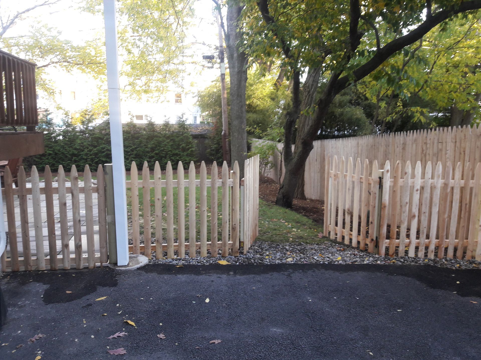 A wooden picket fence surrounds a yard with trees in the background