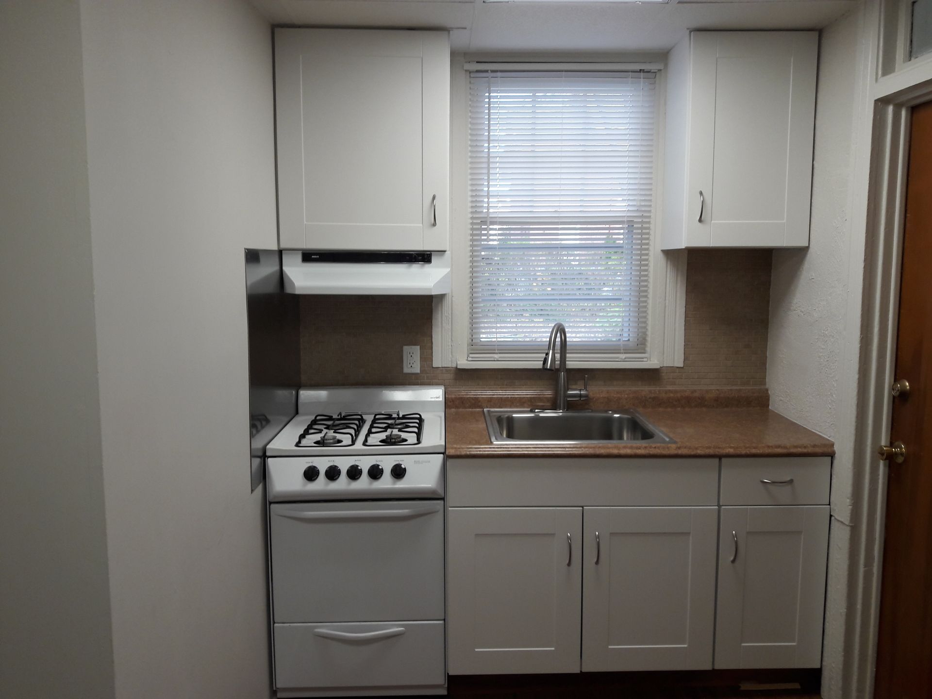 A kitchen with a stove , sink , cabinets and a window.