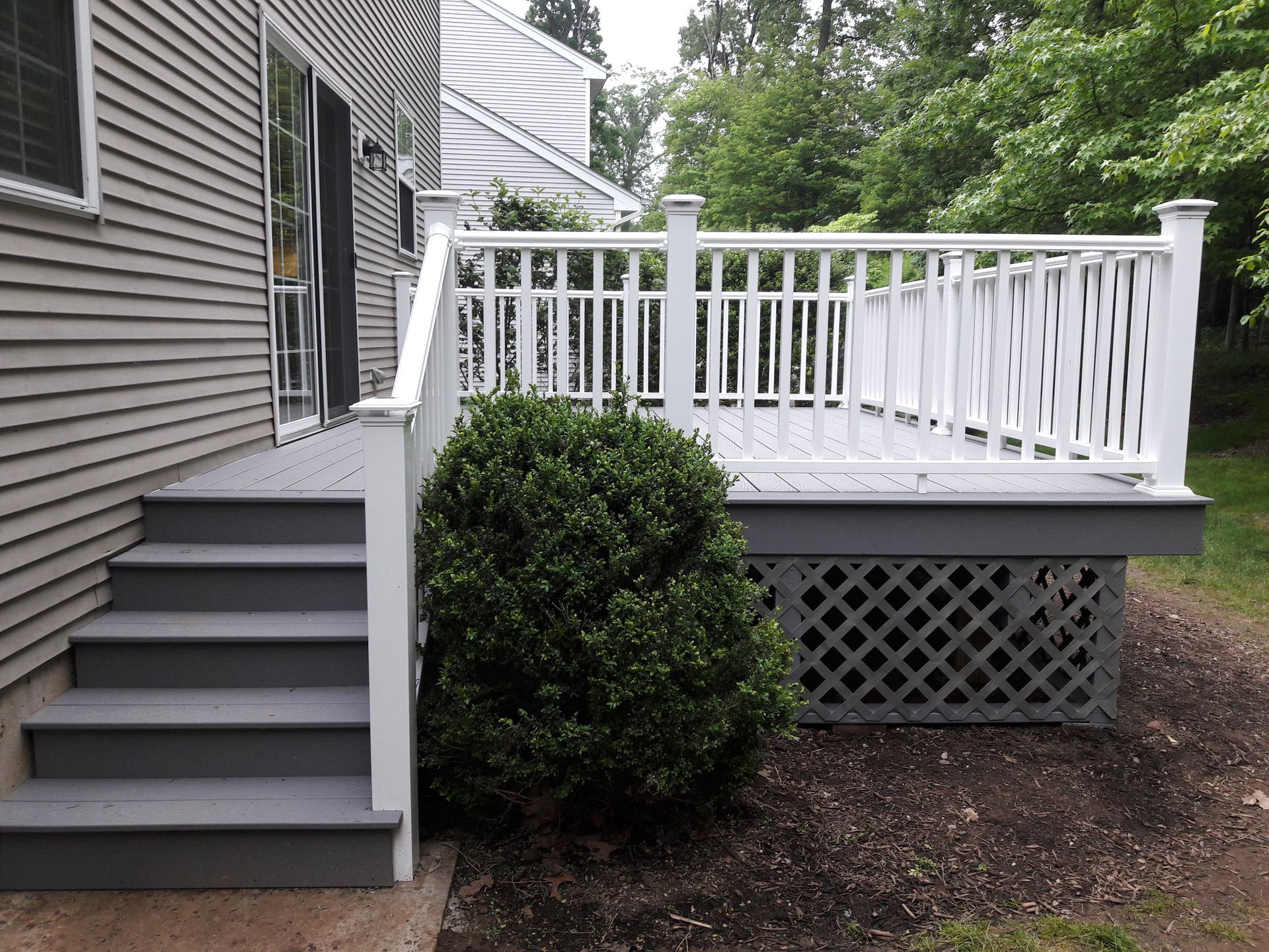 A deck with stairs and a white railing is in front of a house.
