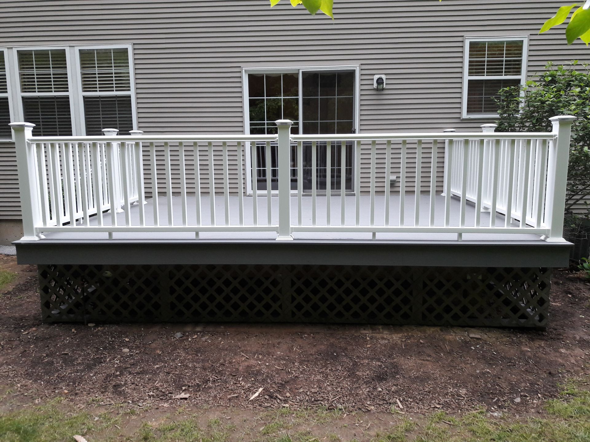 A large deck with a white railing is in front of a house.