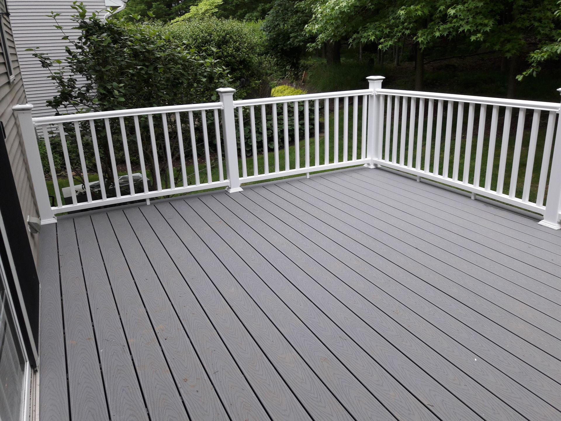 A gray deck with a white railing and trees in the background