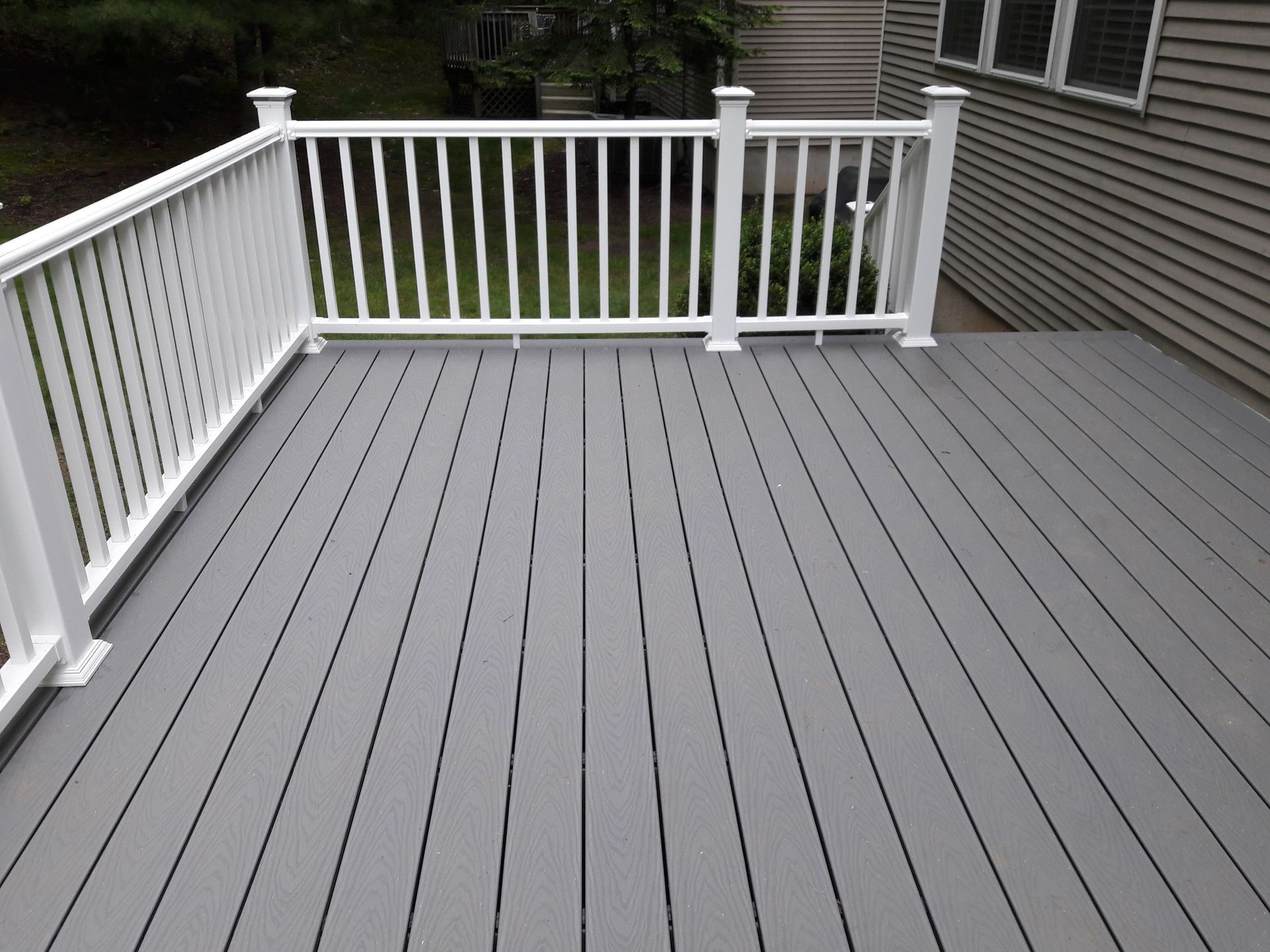 A gray deck with a white railing and a house in the background
