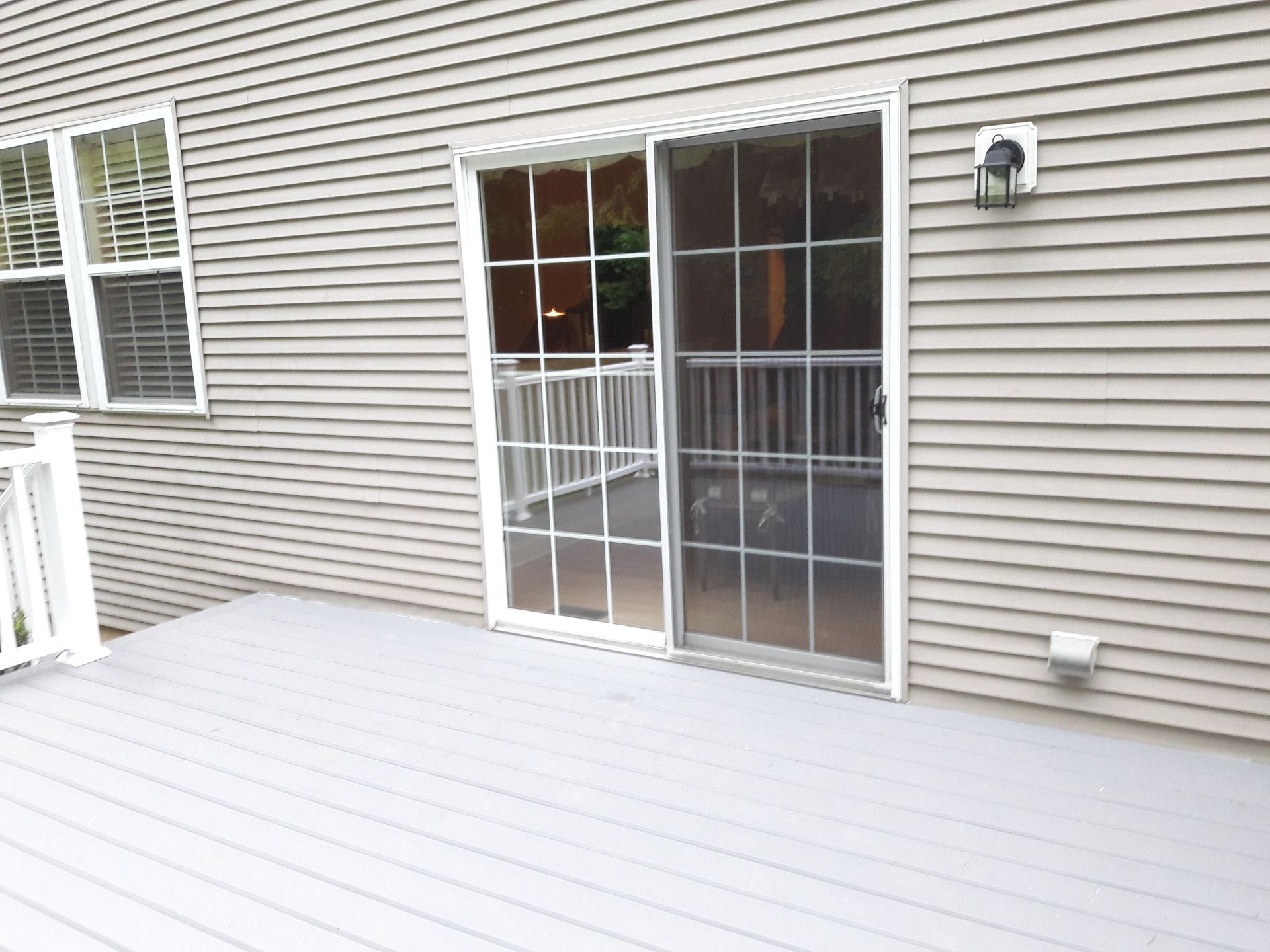 A deck with a sliding glass door in front of a house.