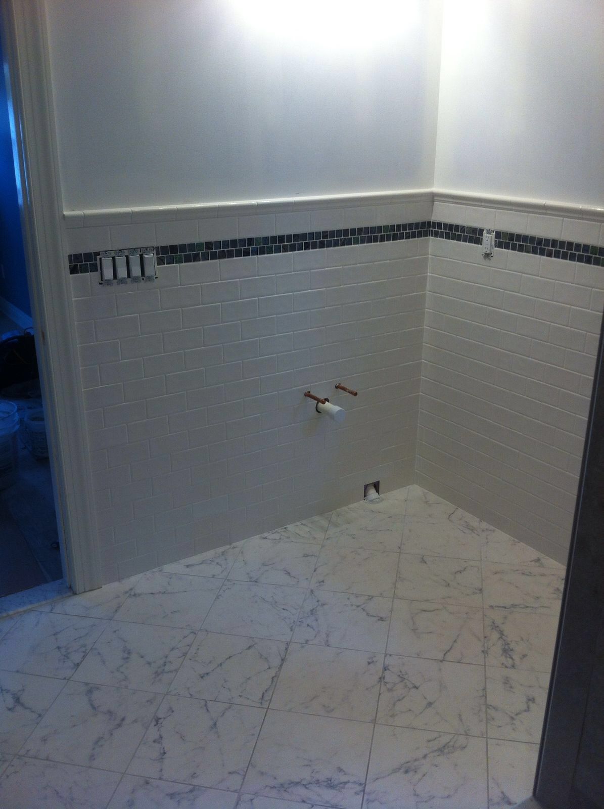 A bathroom with white tiles and a marble floor.