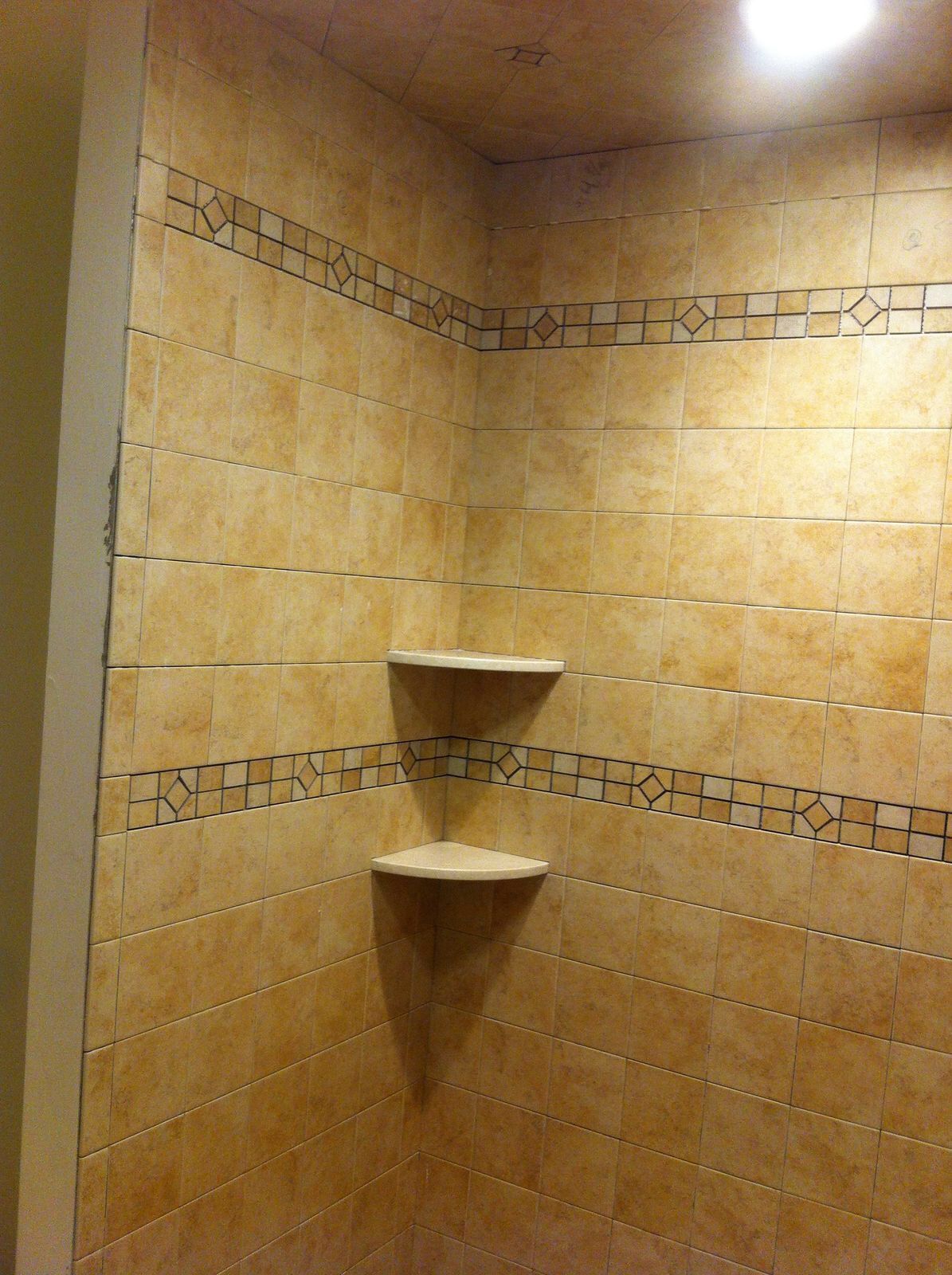 A shower stall with a corner shelf and a stained glass border.