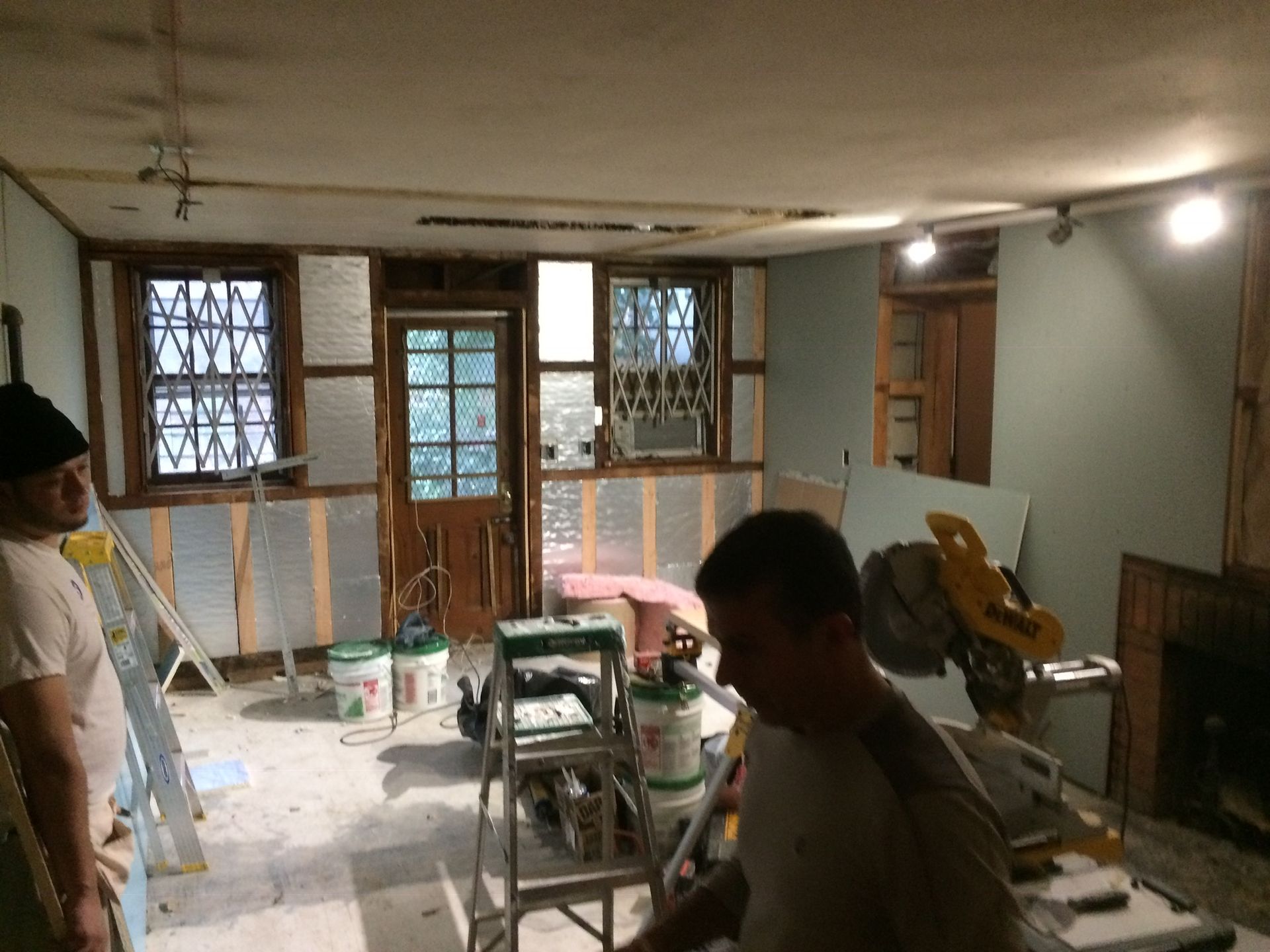 Two men are working in a room with buckets of paint and a ladder