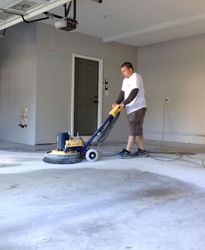 A man is using a machine to clean a concrete floor in a garage.