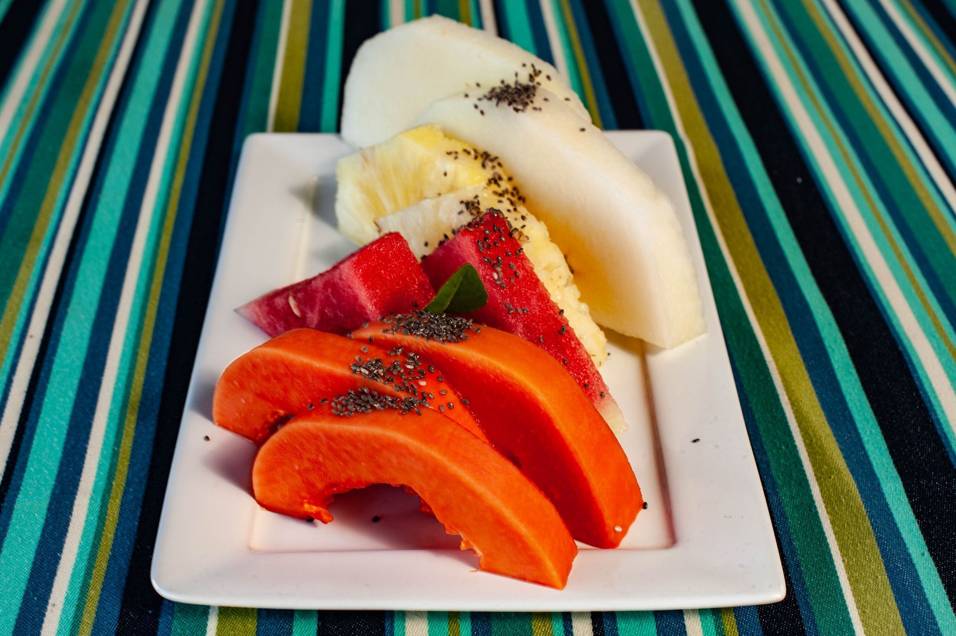 Um prato branco coberto com frutas fatiadas sobre uma toalha de mesa listrada