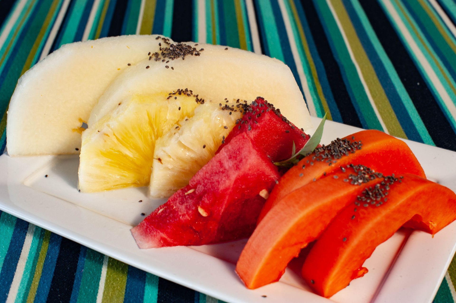 Um prato branco coberto com frutas fatiadas, incluindo abacaxi, melancia e mamão