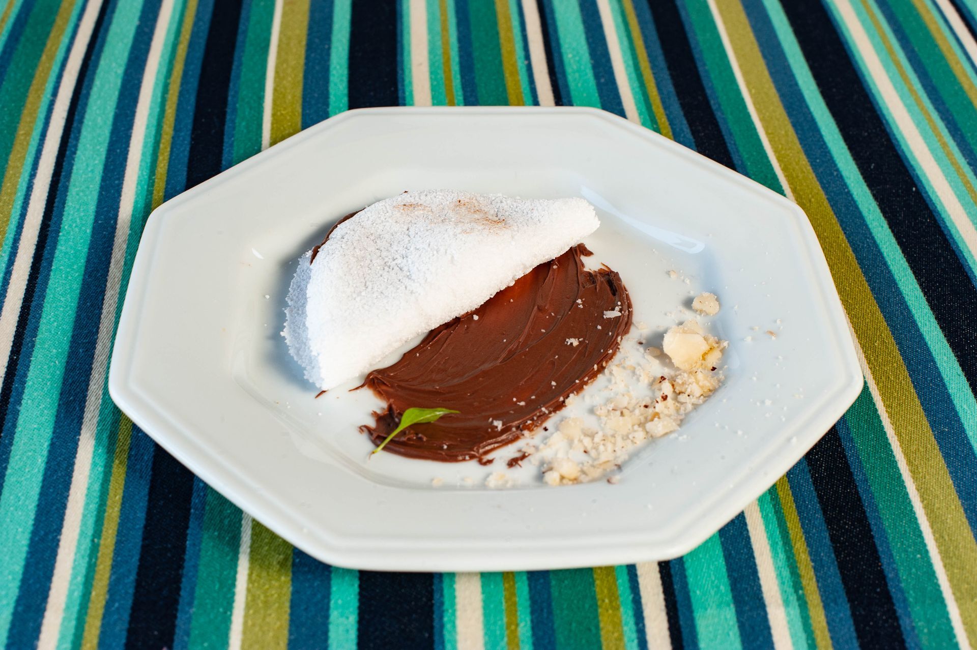 Um prato branco com um pedaço de comida sobre uma toalha de mesa listrada.