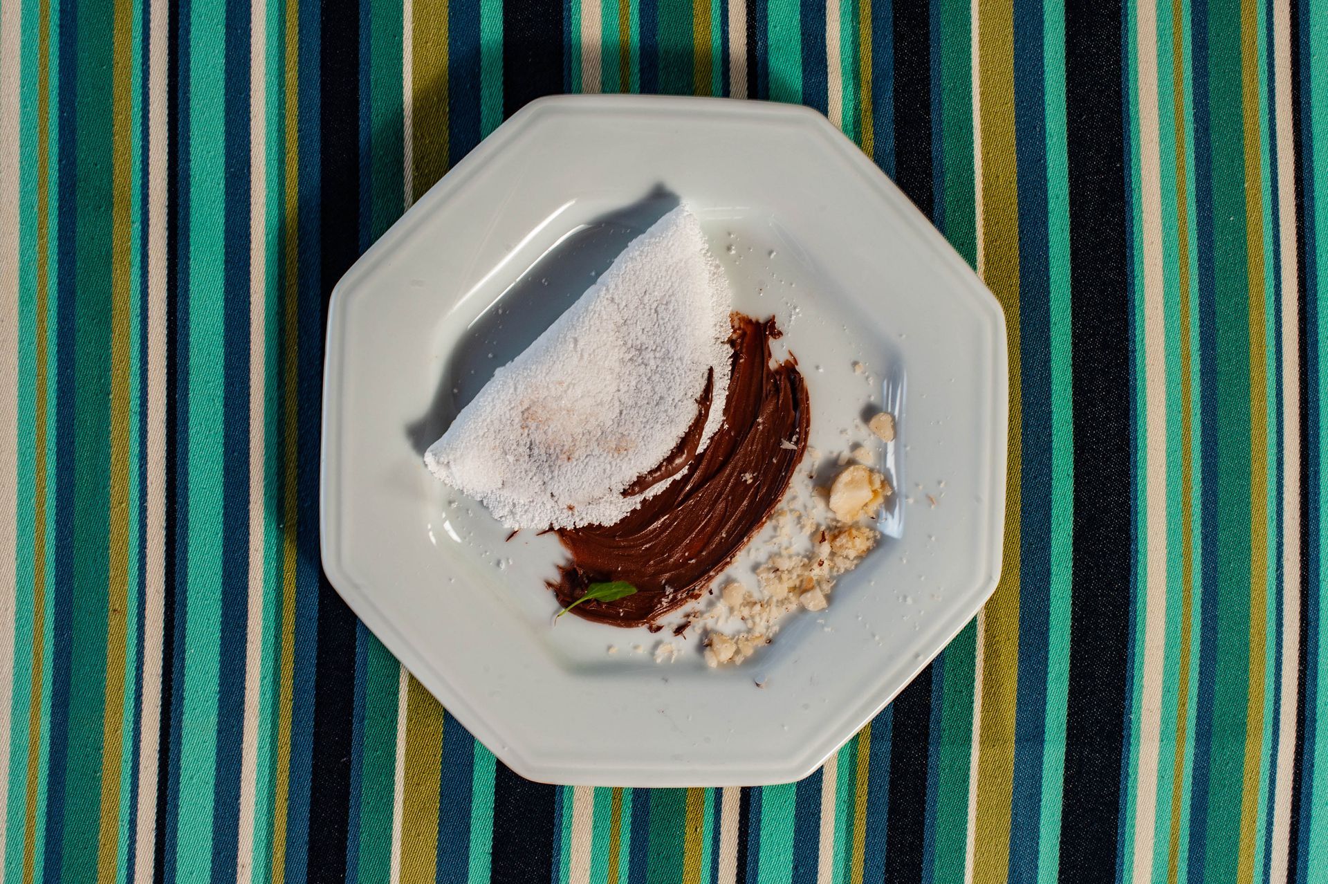 Um prato branco coberto com um pedaço de comida sobre uma toalha de mesa listrada.