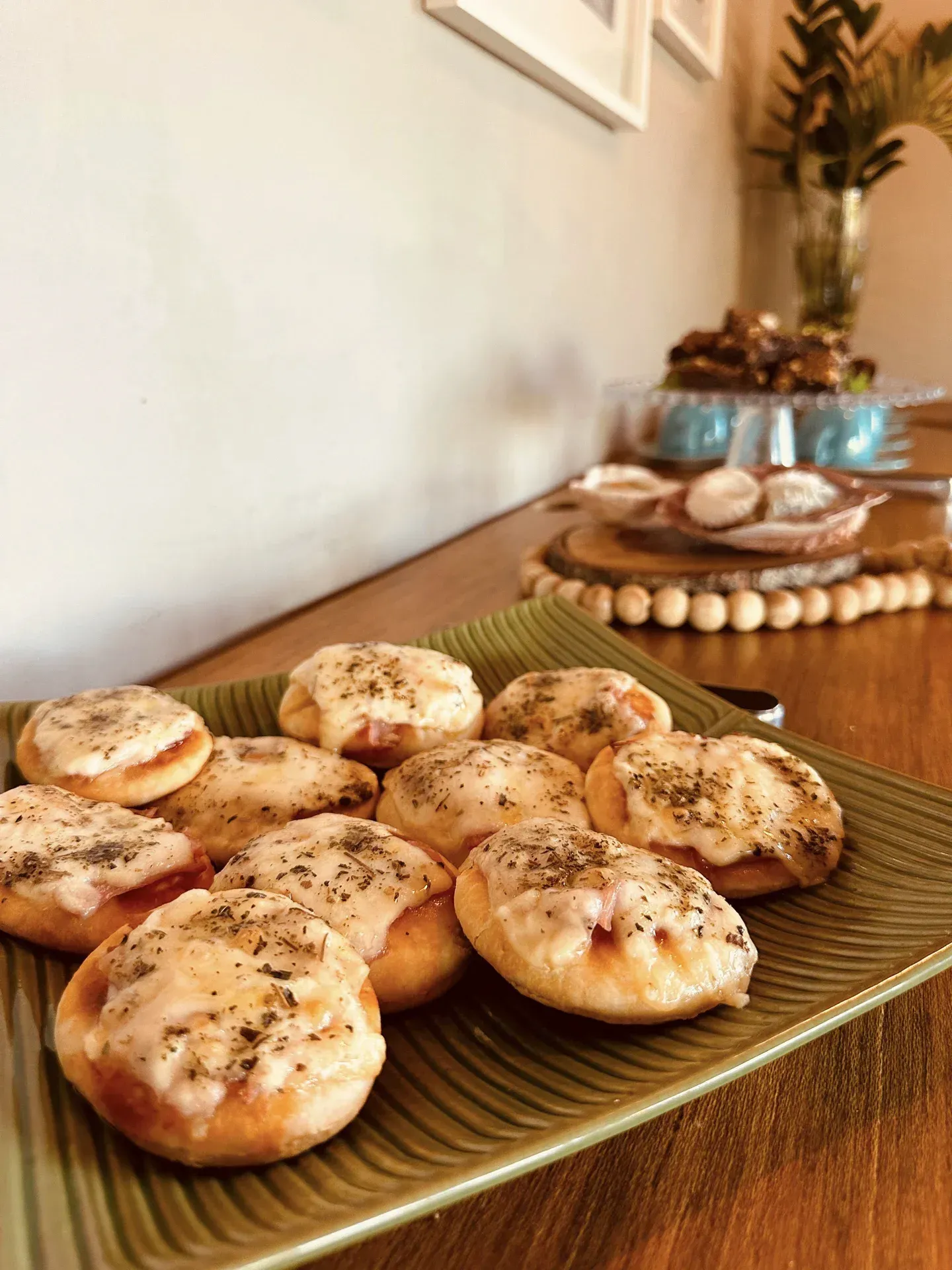 Um prato verde coberto com mini pizzas em uma mesa de madeira.