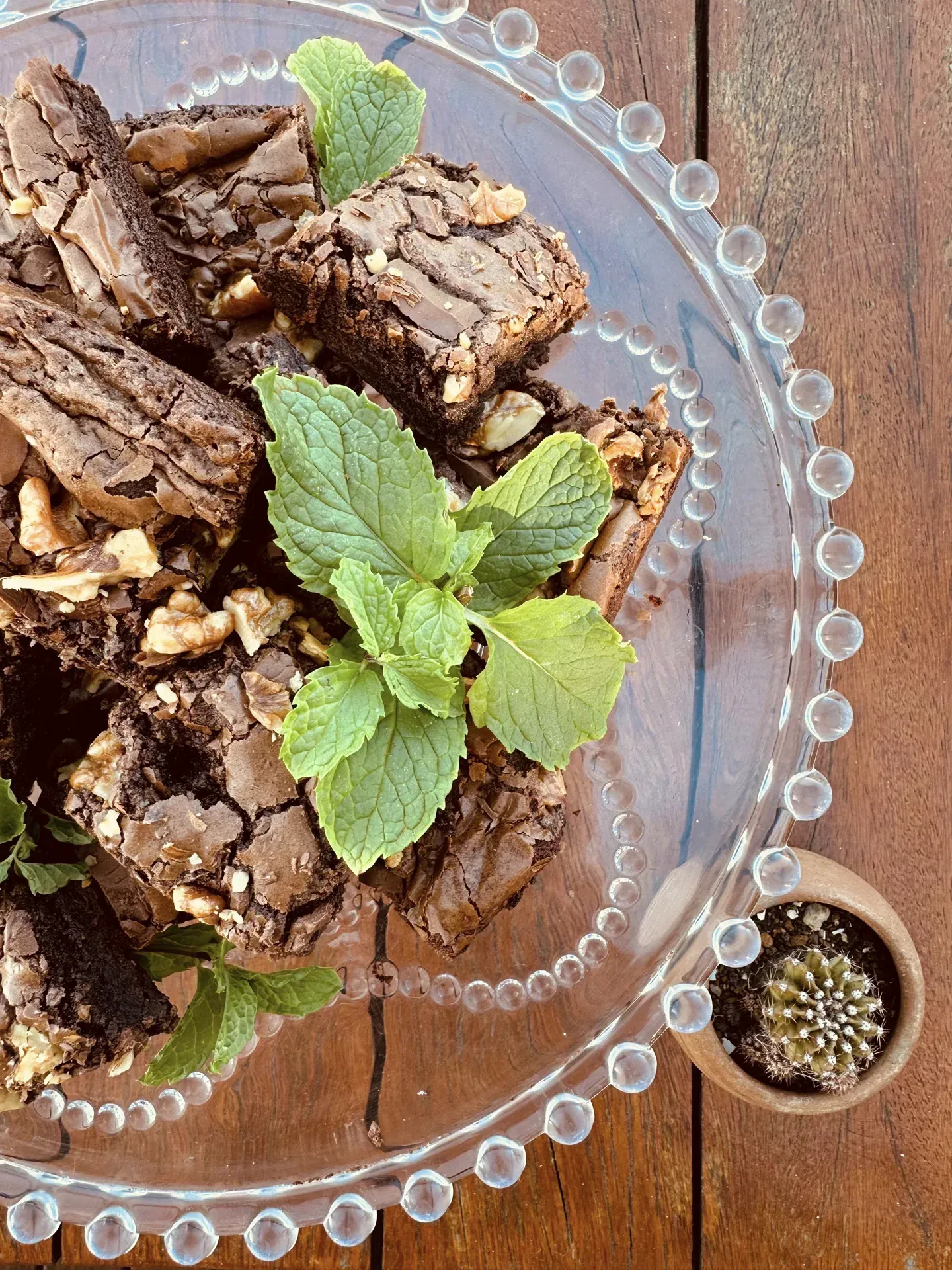 Um prato de vidro coberto com brownies e folhas de hortelã sobre uma mesa de madeira.