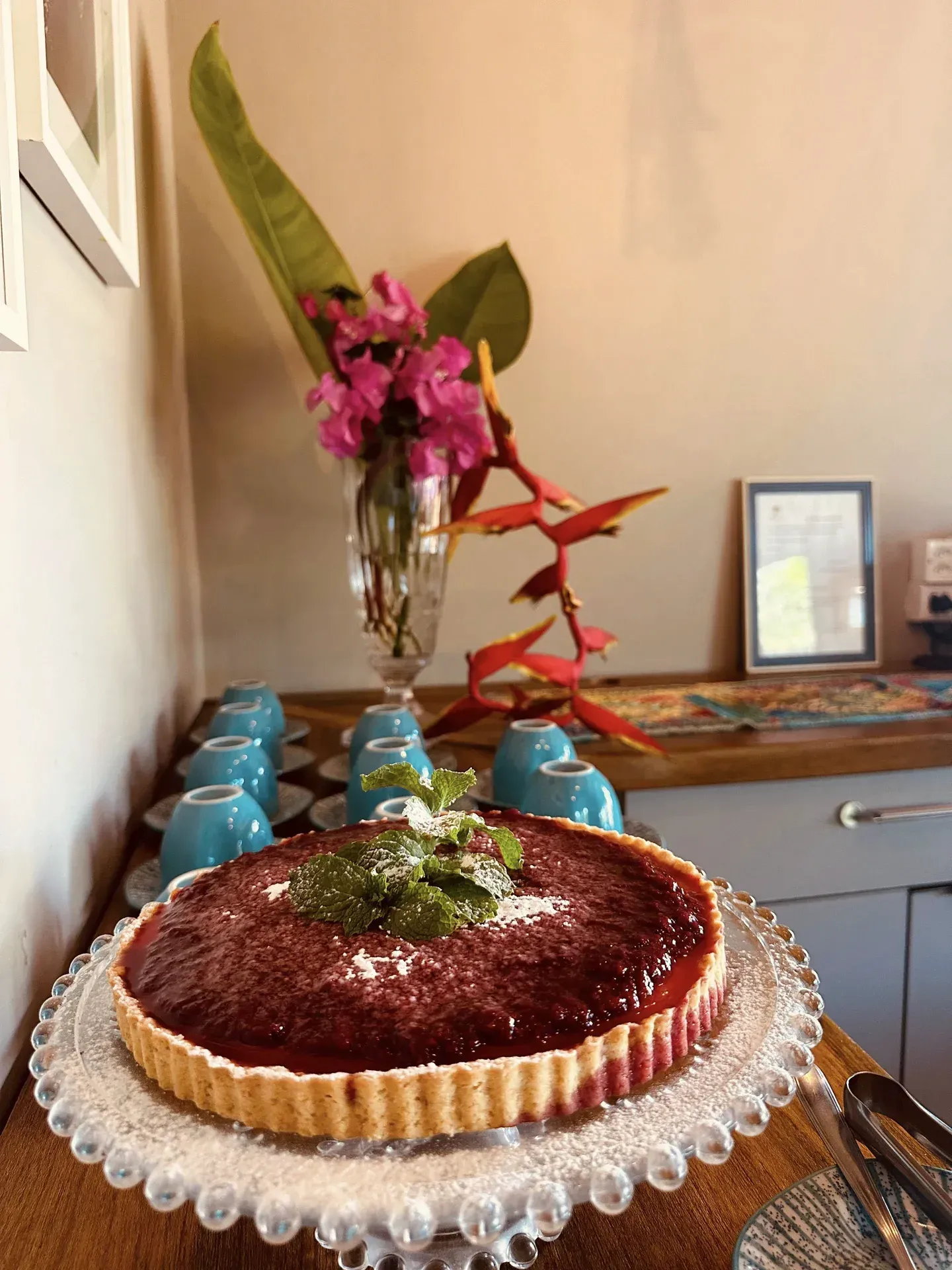 Uma torta em um prato de vidro com um vaso de flores ao fundo