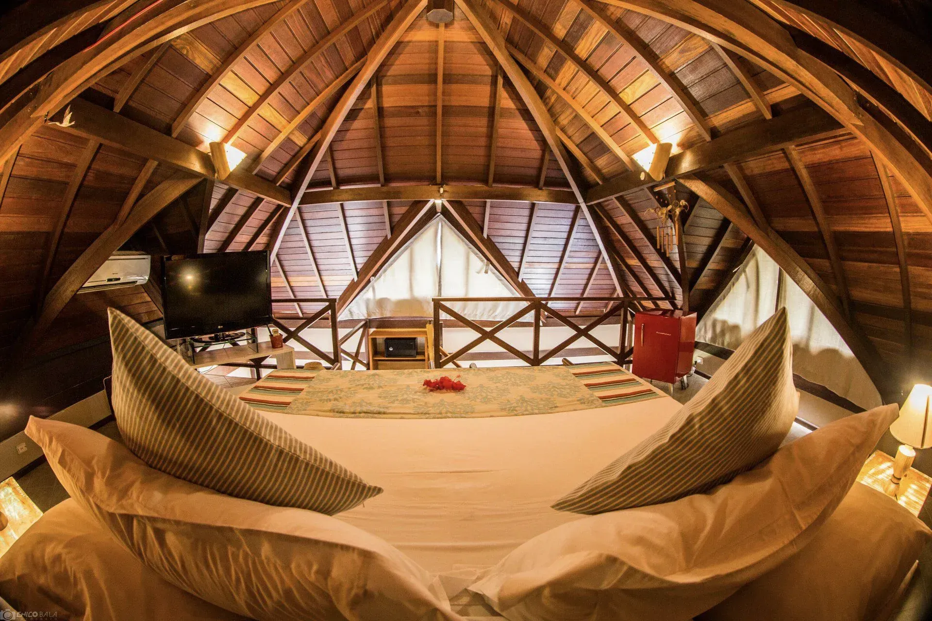 Há uma cama grande no sótão com teto de madeira.